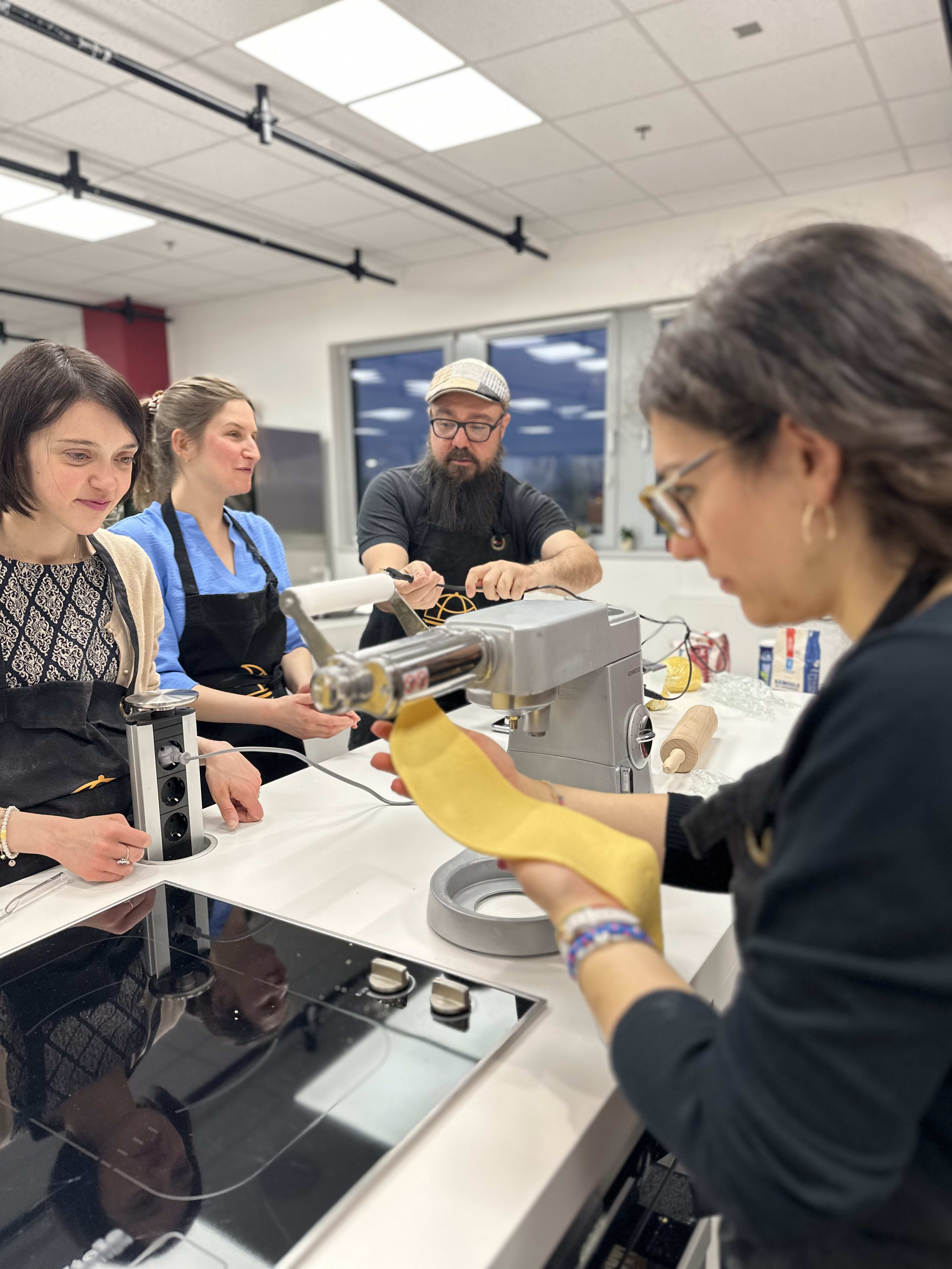 Group of people making fresh pasta with a pasta machine in a cooking class