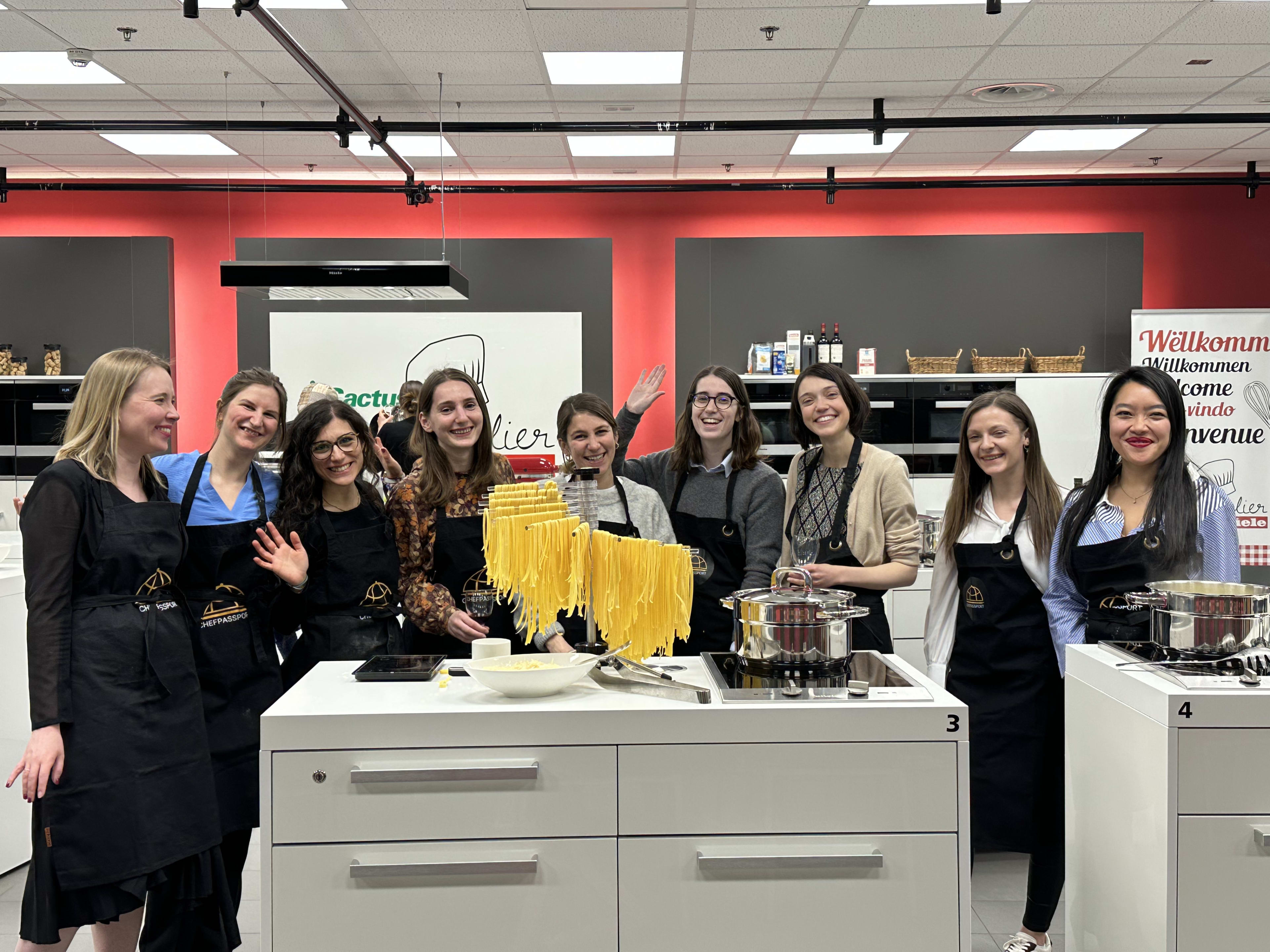 Group of women in aprons making fresh pasta at cooking class station