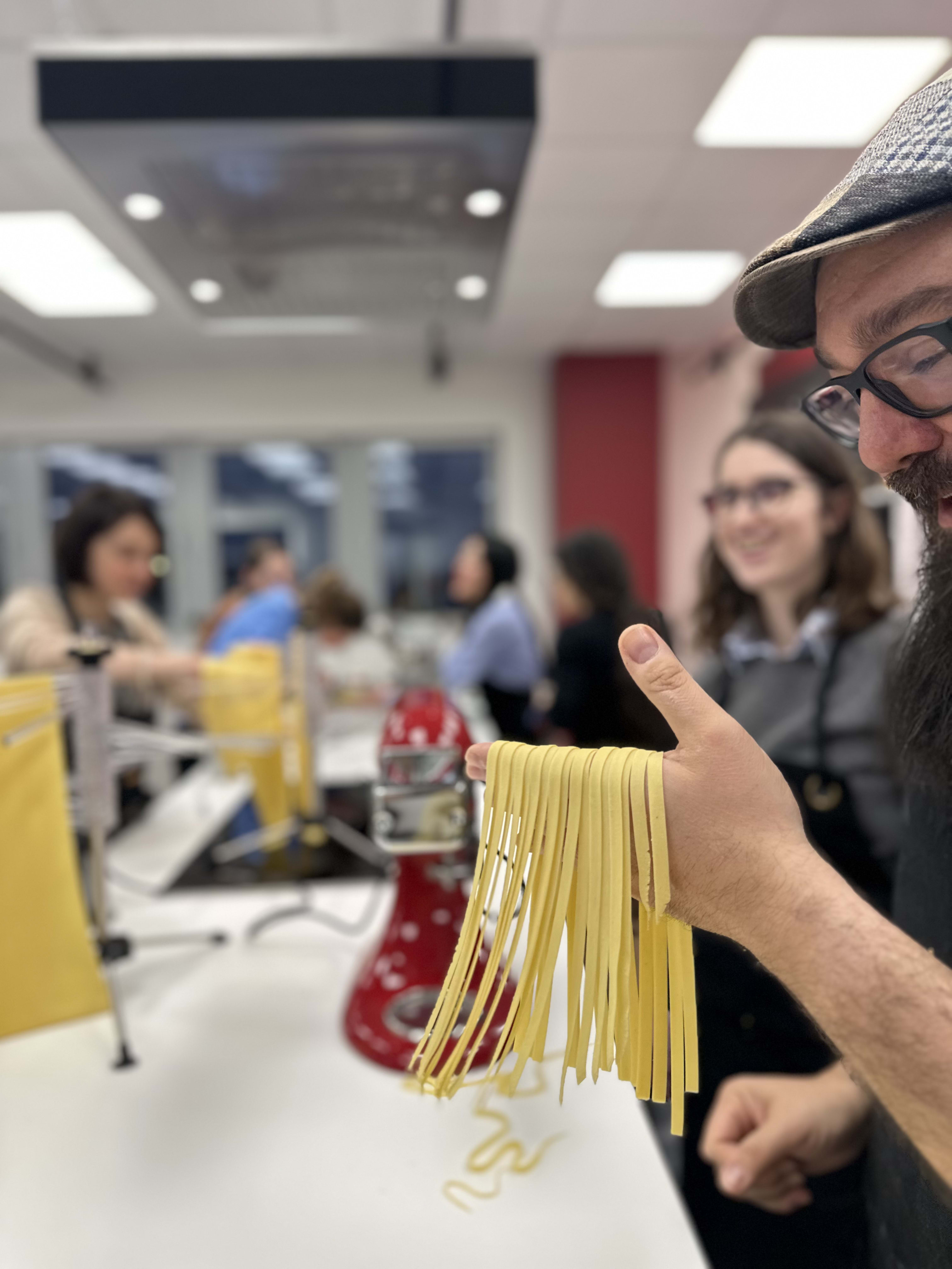 Man in glasses and cap holding freshly made pasta strands in cooking class