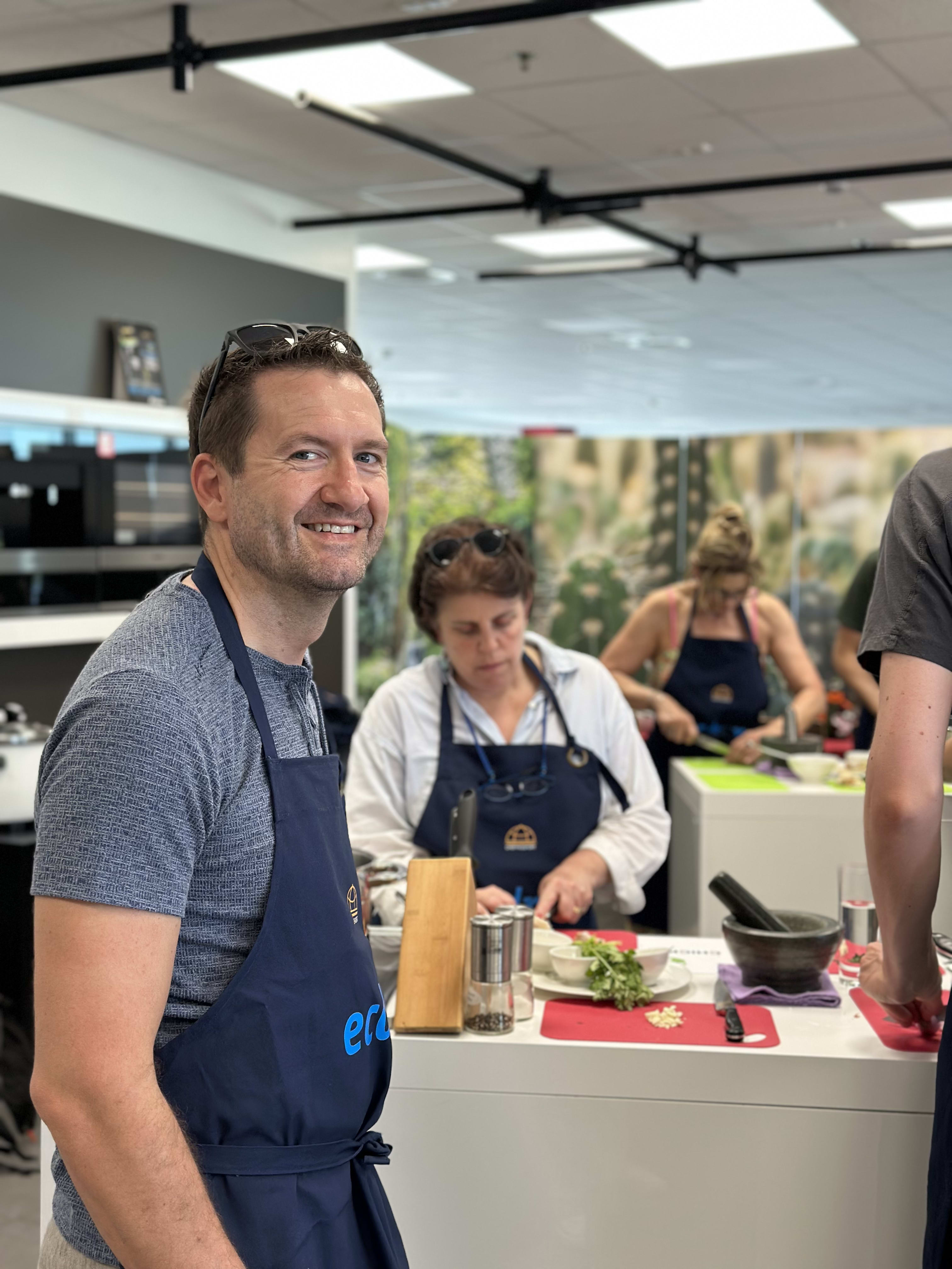 Man in blue apron smiling at camera during a cooking class in modern kitchen