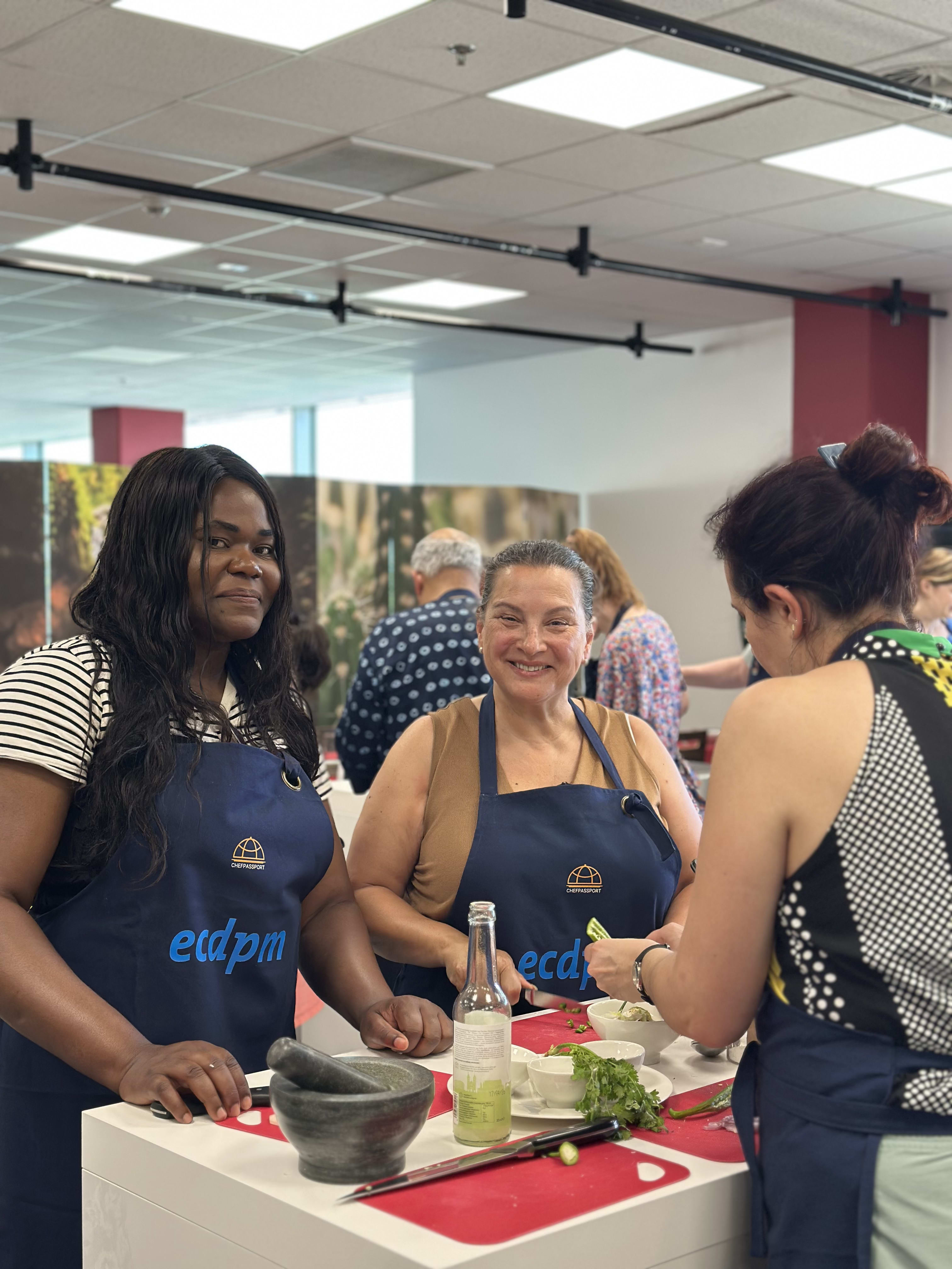 Three women in blue aprons preparing food at a cooking class event