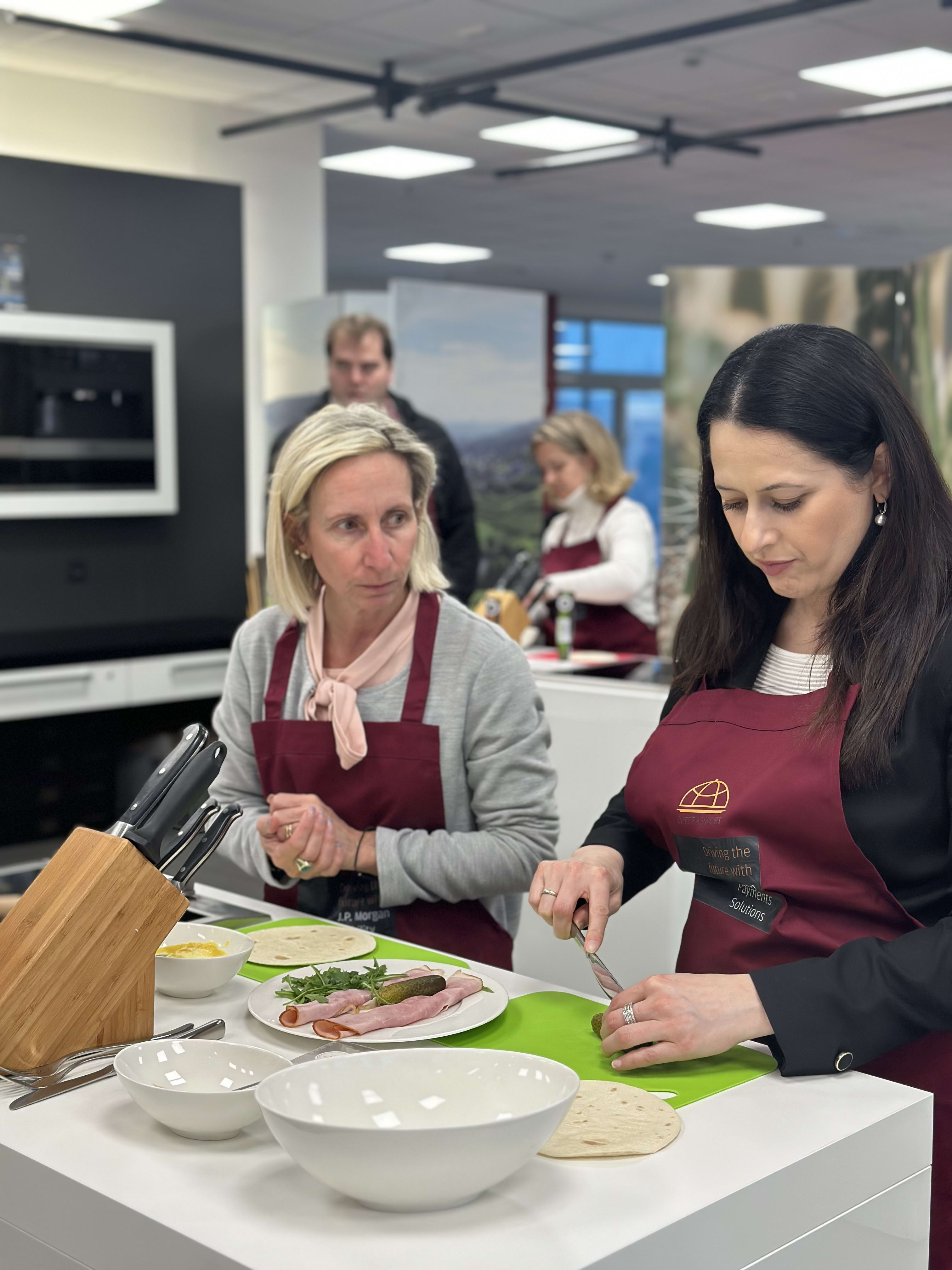 Two women in burgundy aprons preparing food at a cooking class in modern kitchen