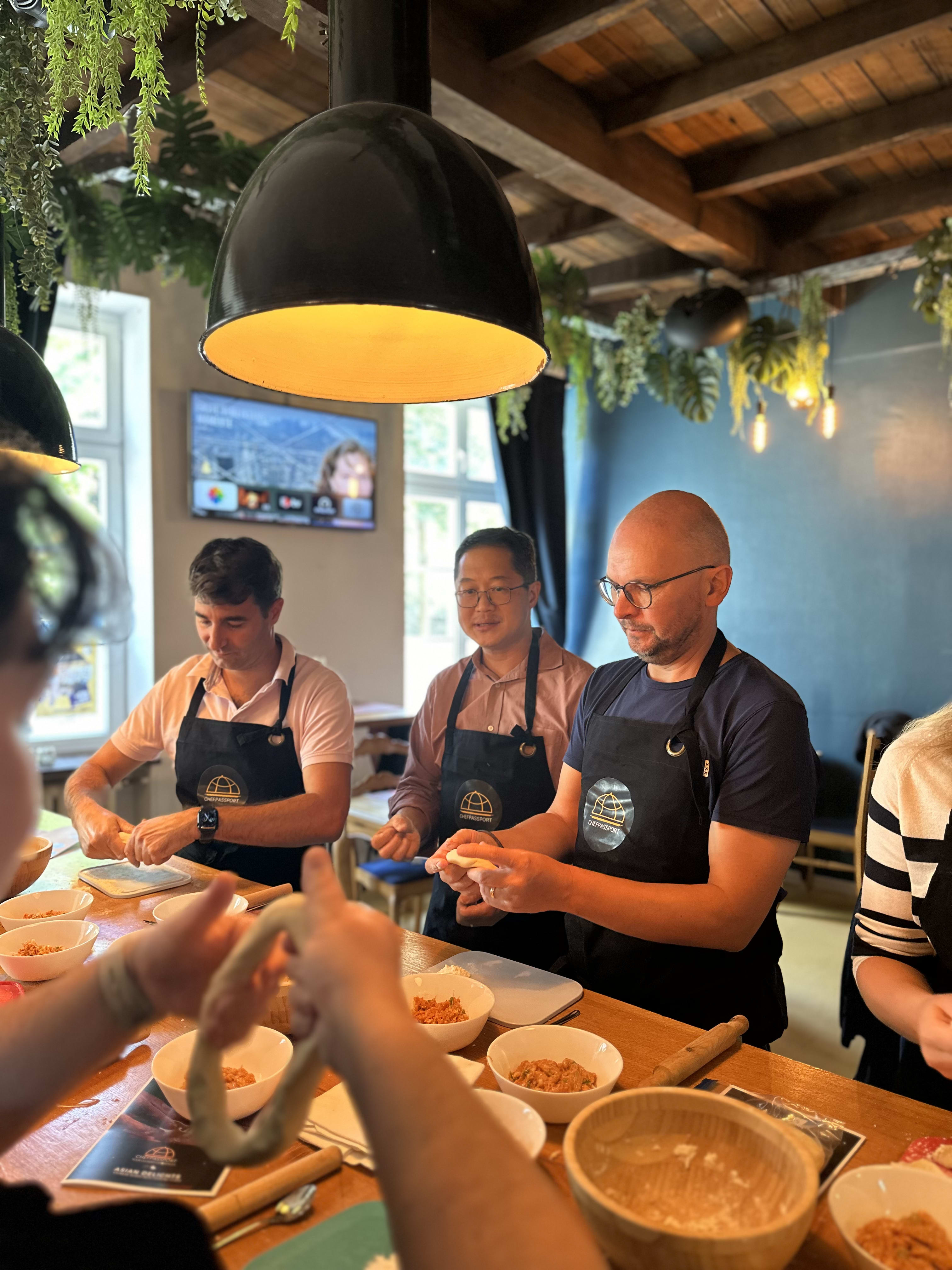 Group of people in black aprons participating in a hands-on cooking class at a rustic restaurant