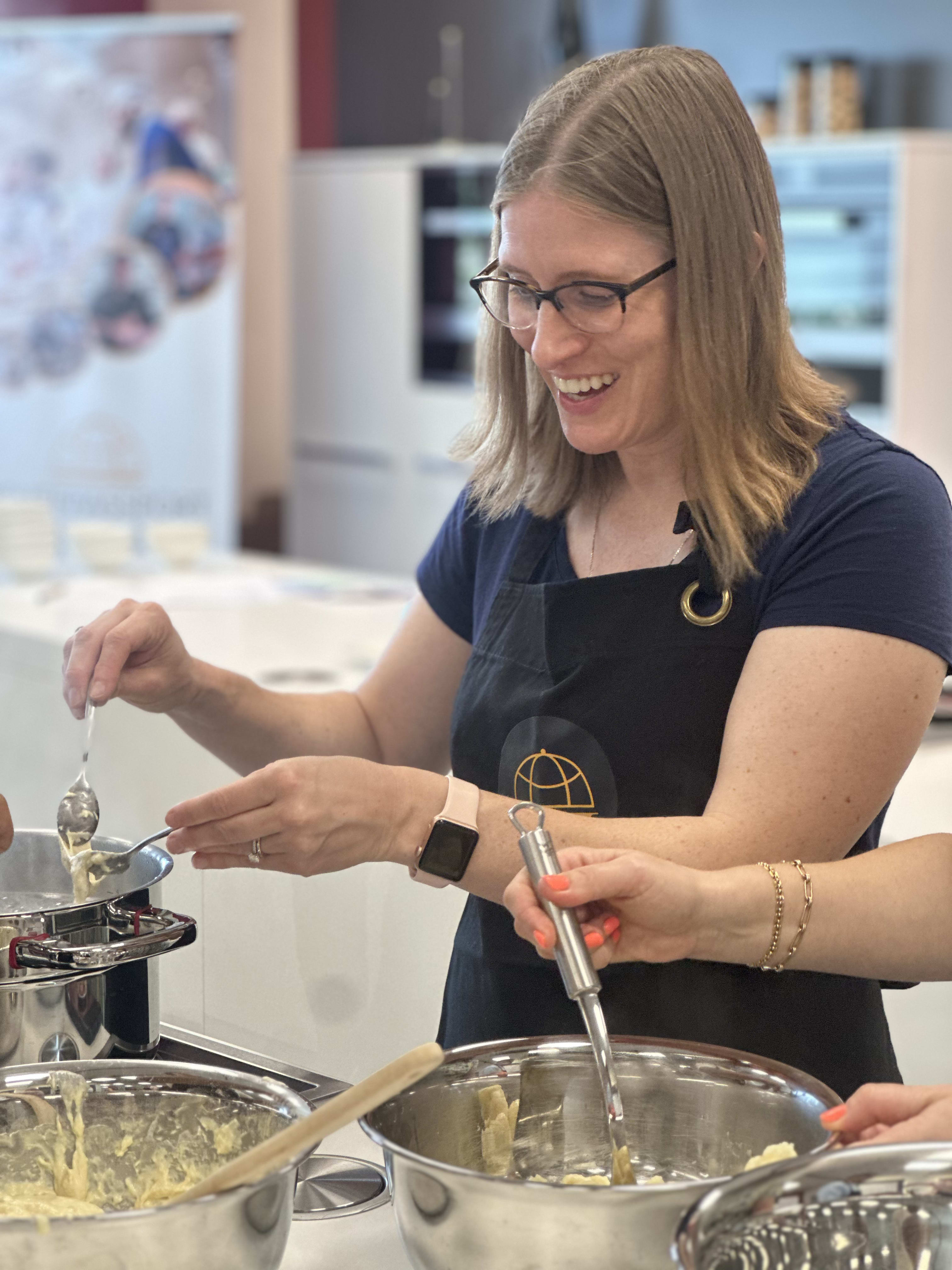 Woman wearing glasses and apron smiling while cooking with metal bowls in kitchen