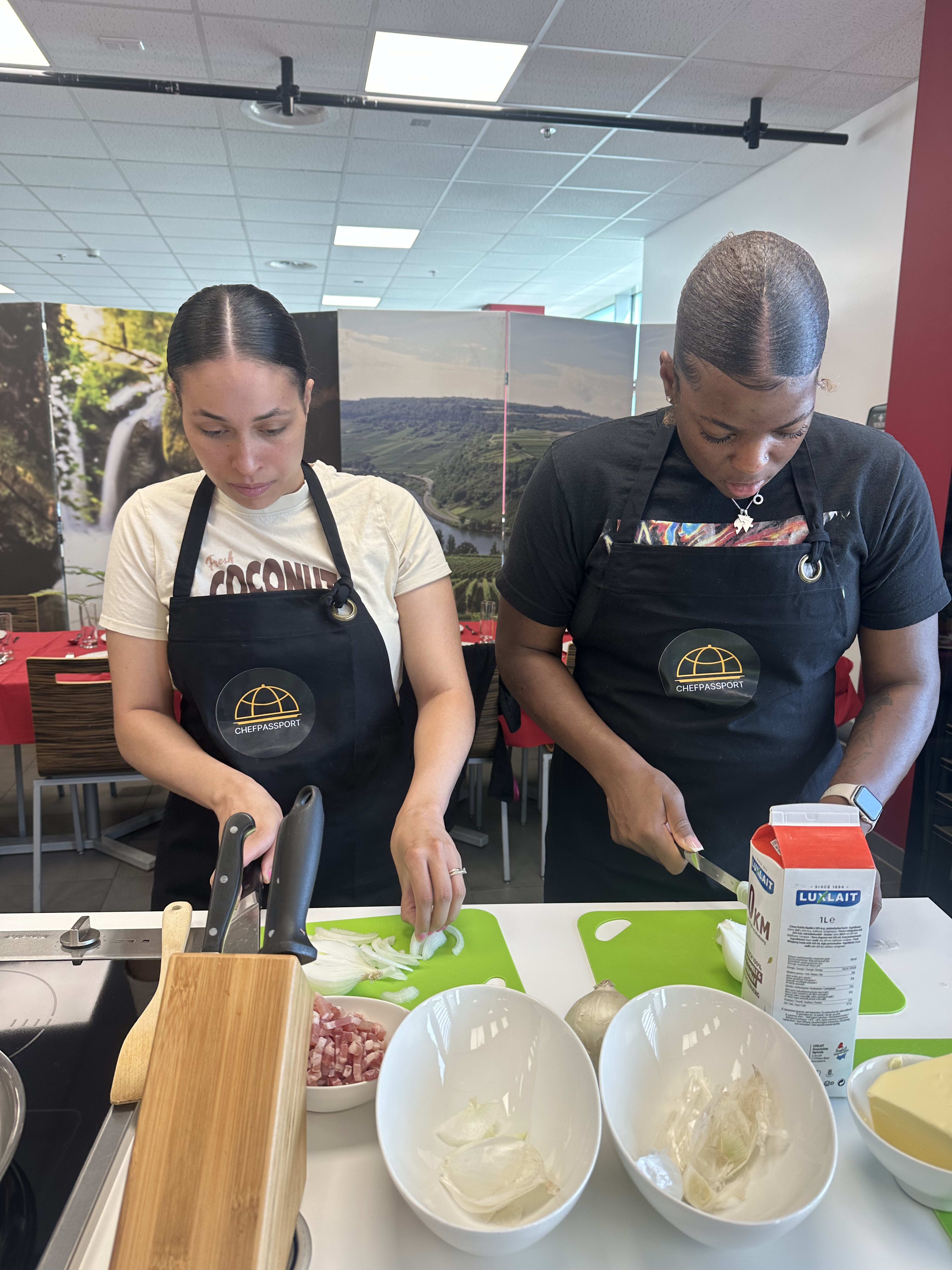 Two women in Chef's Passport aprons preparing ingredients at cooking class station