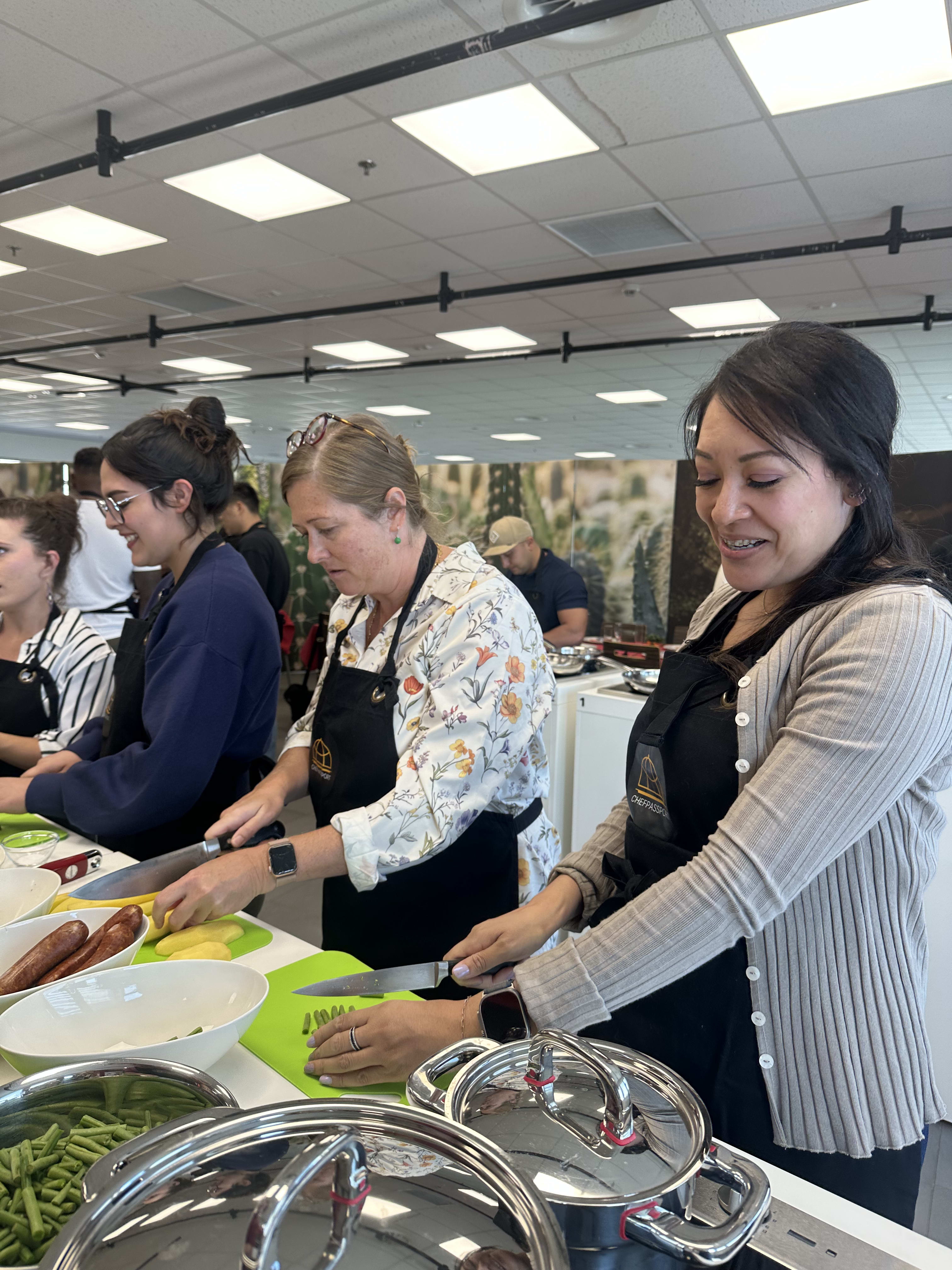 Three women in aprons preparing food at cooking class with ingredients on counter
