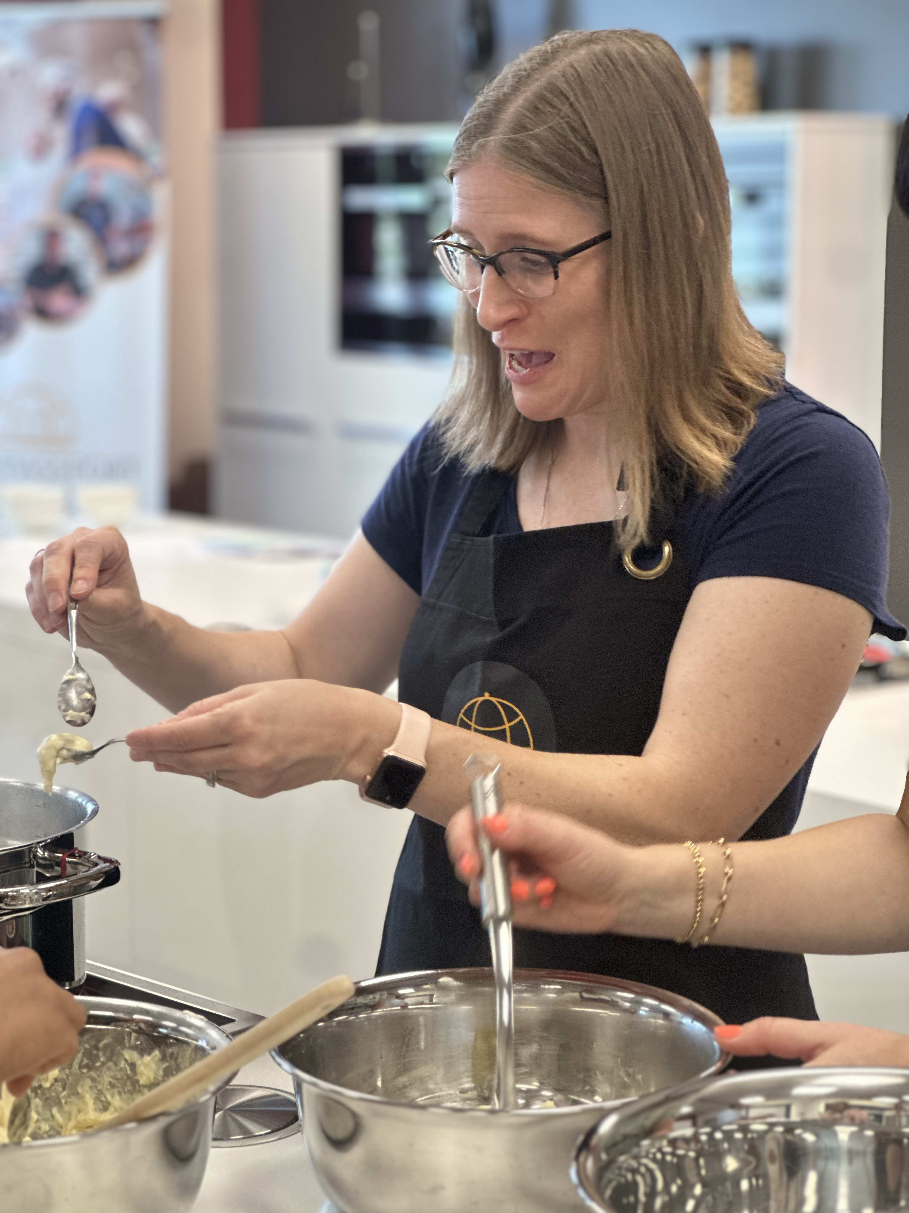 Woman with glasses wearing black apron cooking and stirring ingredients in stainless steel pot