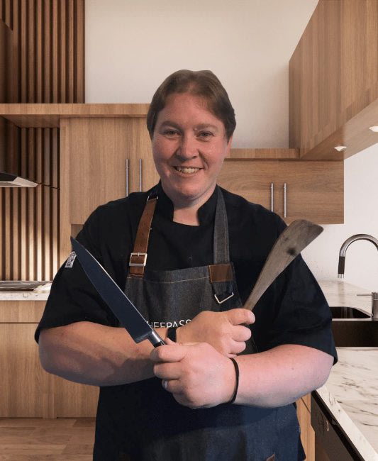 Professional chef in black apron holding two large kitchen knives in modern kitchen