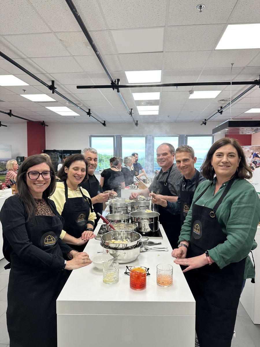 Six professionals in aprons cooking together at white station with steel pots