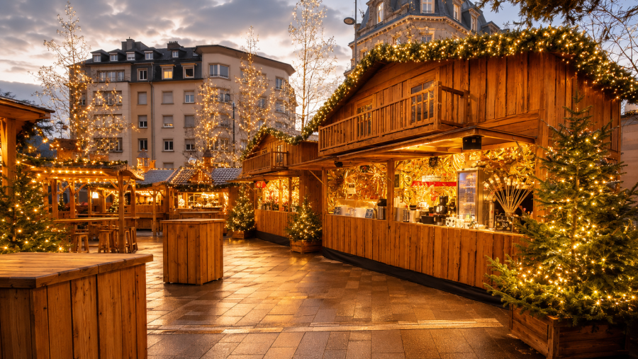 Illuminated Christmas market wooden chalets with festive lights at dusk in European town square