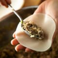 Hands filling dumpling wrapper with savory meat and vegetable mixture