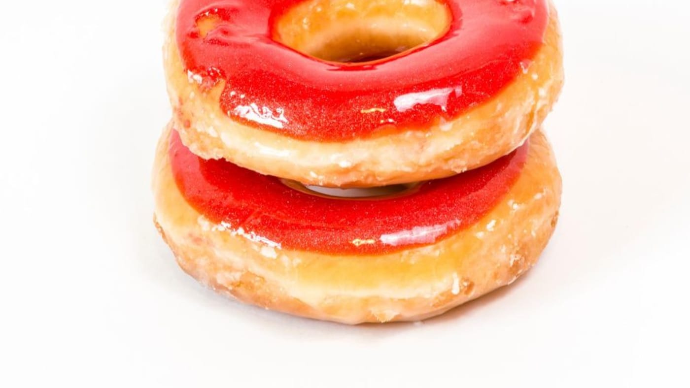 Two stacked glazed donuts with shiny red strawberry icing on white background