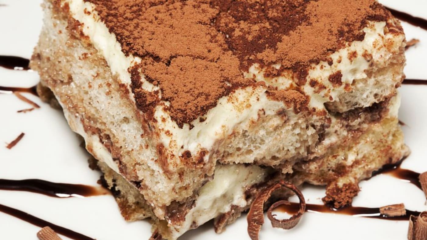 Layered tiramisu dessert with cocoa powder and chocolate shavings on white plate