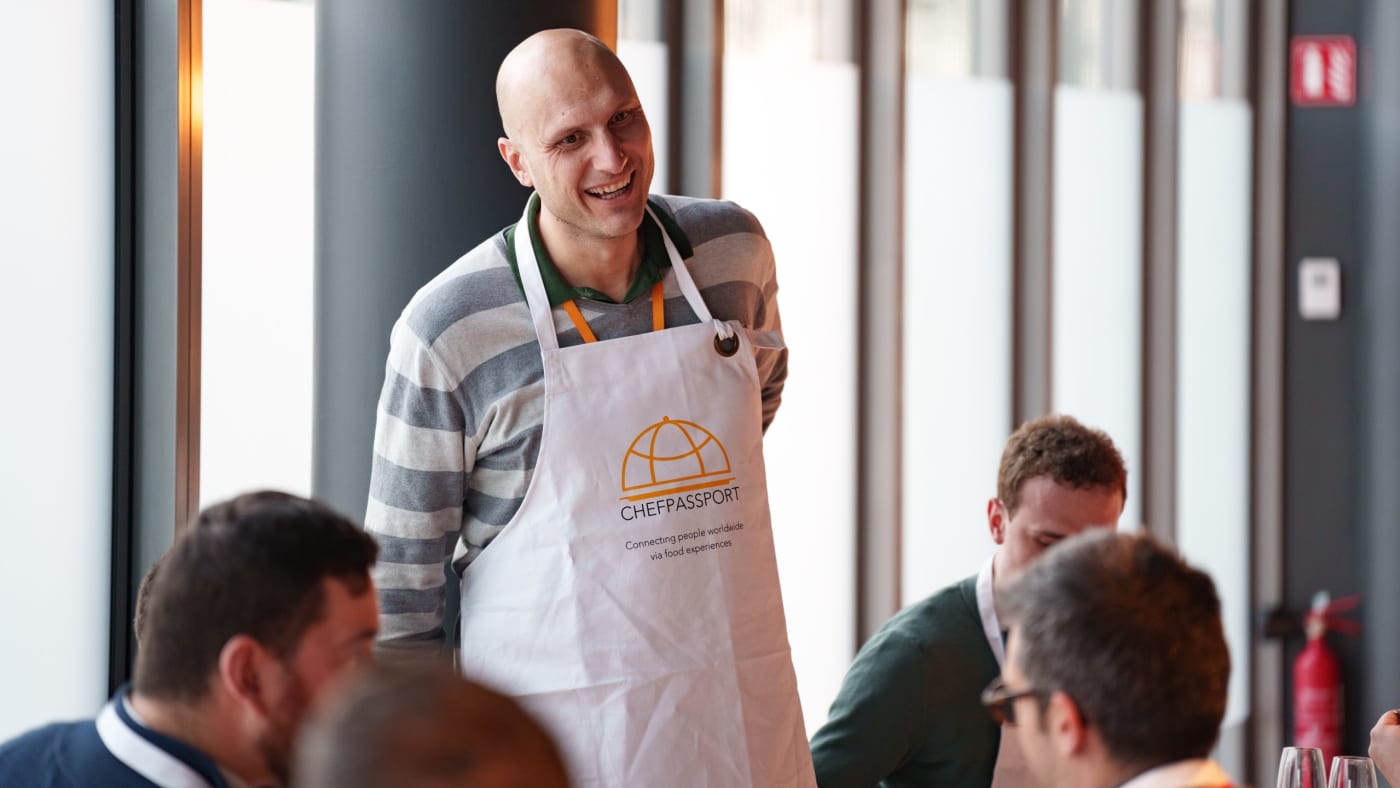 Diverse cooking class participants wearing aprons smiling at tables in bright Luxembourg venue
