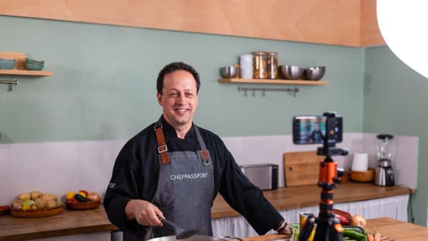 Chef in black uniform and apron smiling while filming cooking video in modern kitchen