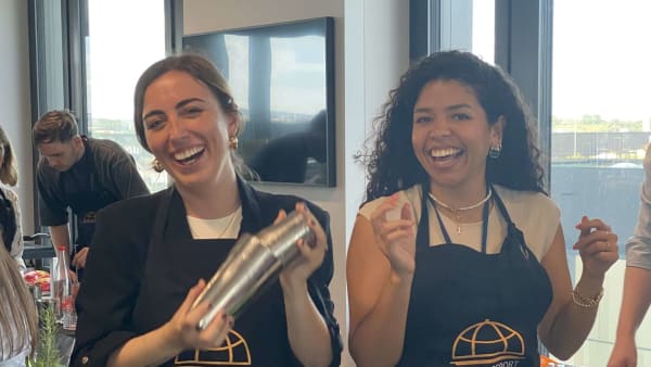 Diverse cooking class participants wearing aprons smiling at tables in bright Luxembourg venue