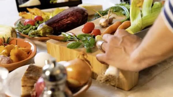 Fresh vegetables leeks carrots eggplant mushrooms spilling from paper bag on wooden cutting board