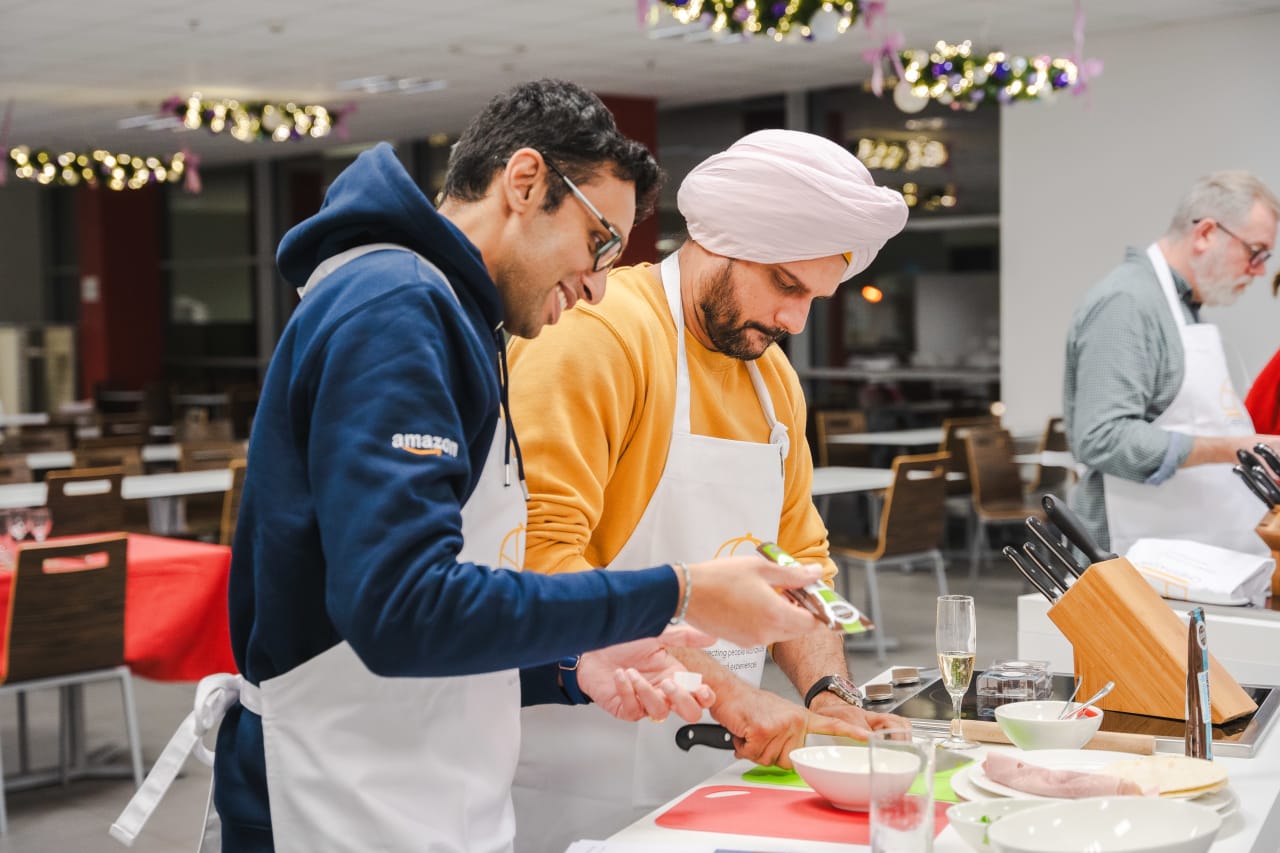 Two men in aprons cooking together in modern kitchen during culinary class
