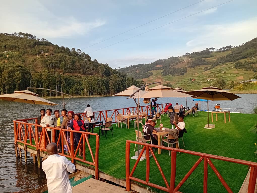 Tourists standing on the dock at Bunyonyi Luxury Resort, peacefully watching the evening reflections on Lake Bunyonyi.