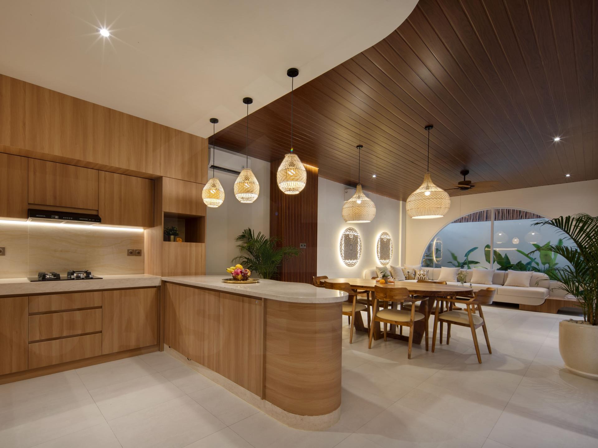 Warm open-plan kitchen, dining, and living area with wood finishes and pendant lighting in a modern Bali villa