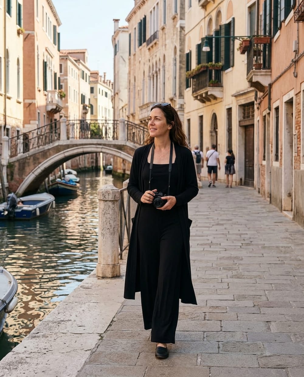 A woman in a black wrinkle-free travel set and long duster cardigan walking a Venice canal street