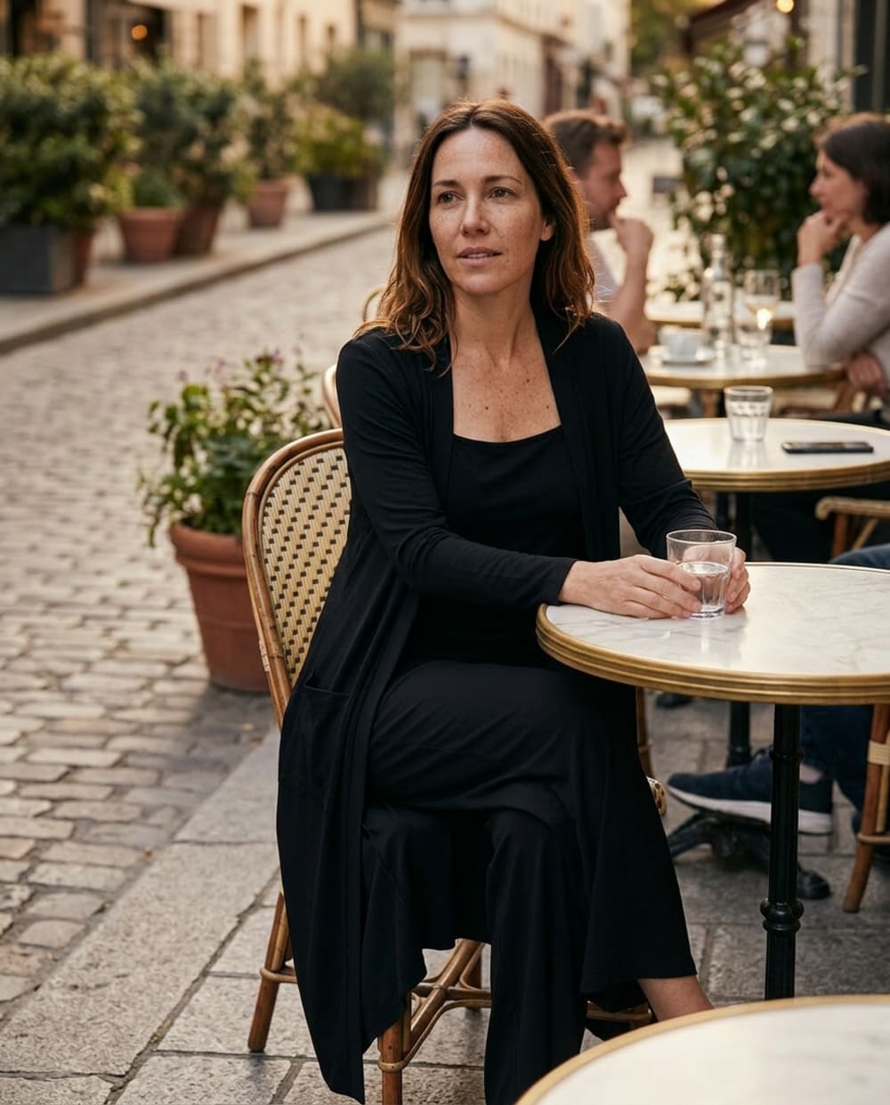 A woman in the black set with the cardigan worn open, seated at a cafe table in the evening