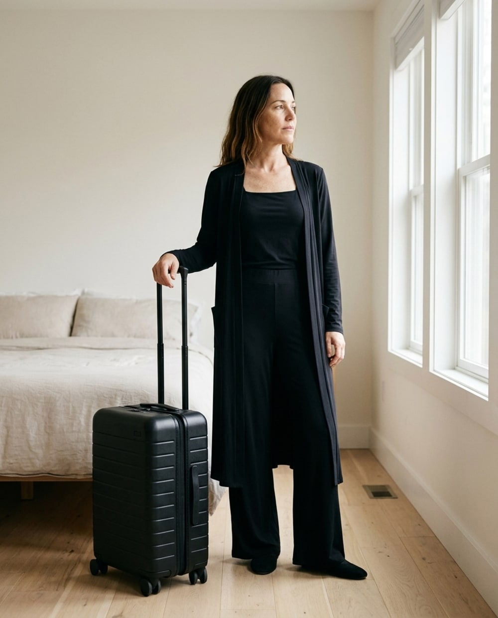 A woman in the black travel set standing with a packed carry-on, ready to leave