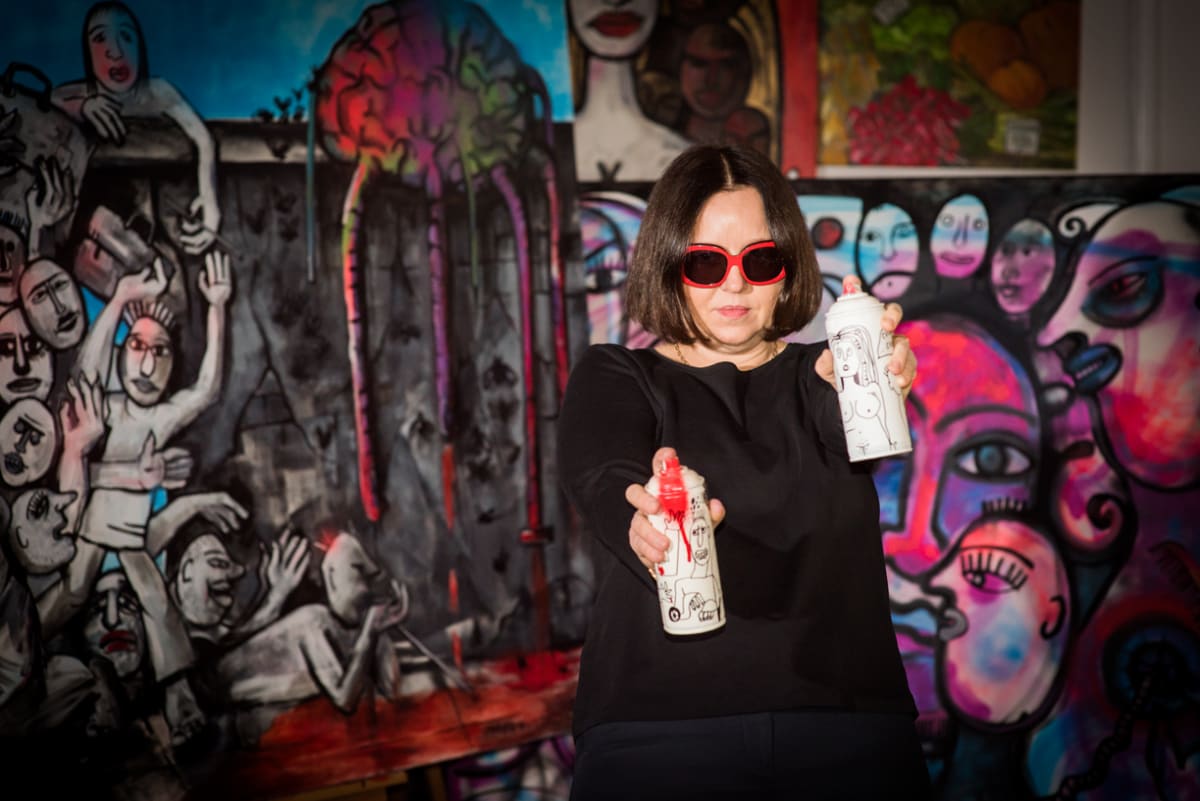 Iwona Siwek-Front holding painted spray cans in front of her work