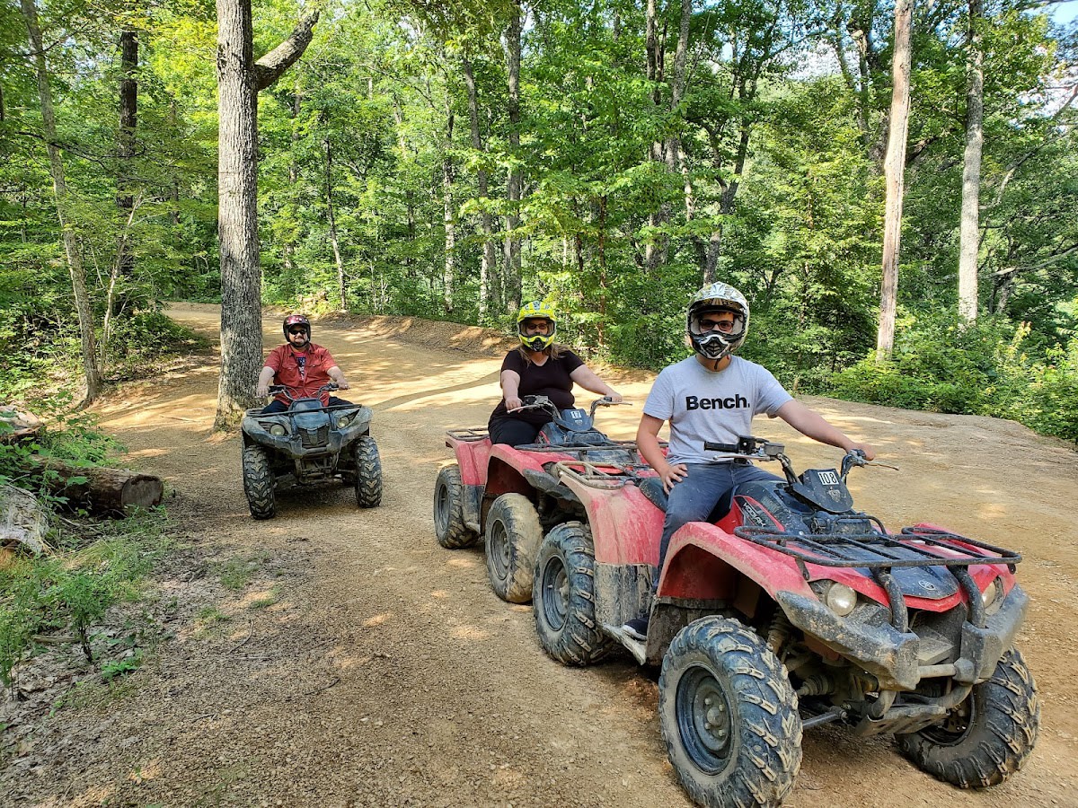 A group of people on ATVs splashing through a muddy trail in the woods.
