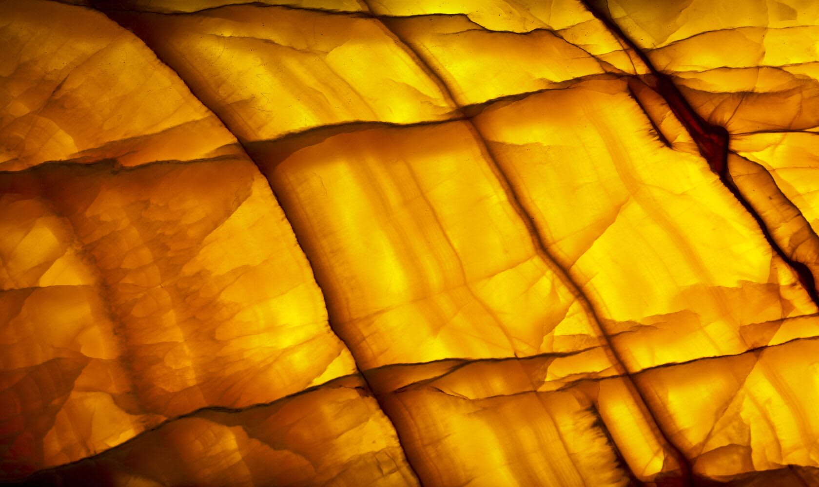 A translucent panel lit from behind, glowing amber and gold, its marbled veining and banding revealed by the backlight — a backlit-onyx effect