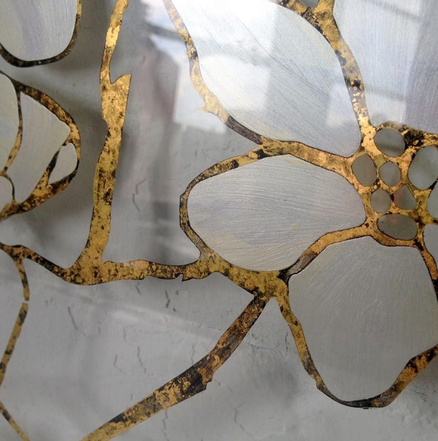 A finished verre églomisé glass panel with a botanical motif — brushed-silver petals outlined and veined in distressed gold leaf on a textured ground