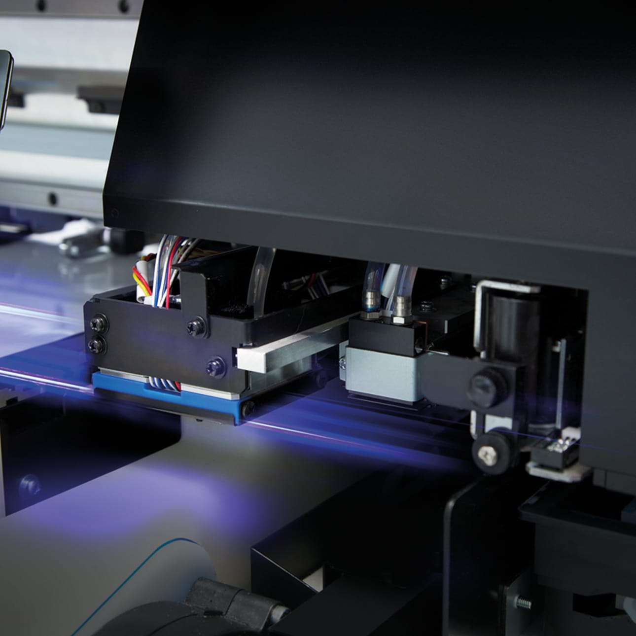 Close-up of a UV flatbed printer carriage, the violet UV-LED lamps glowing as the print head passes over the bed curing ink on the spot