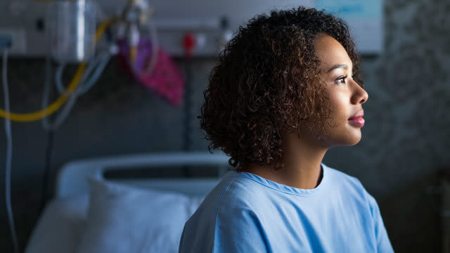 A patient sitting on a hospital bed gazes off into the distance