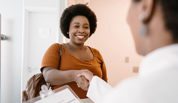 A happy person smiles and shakes hands with a medical professional holding a clipboard