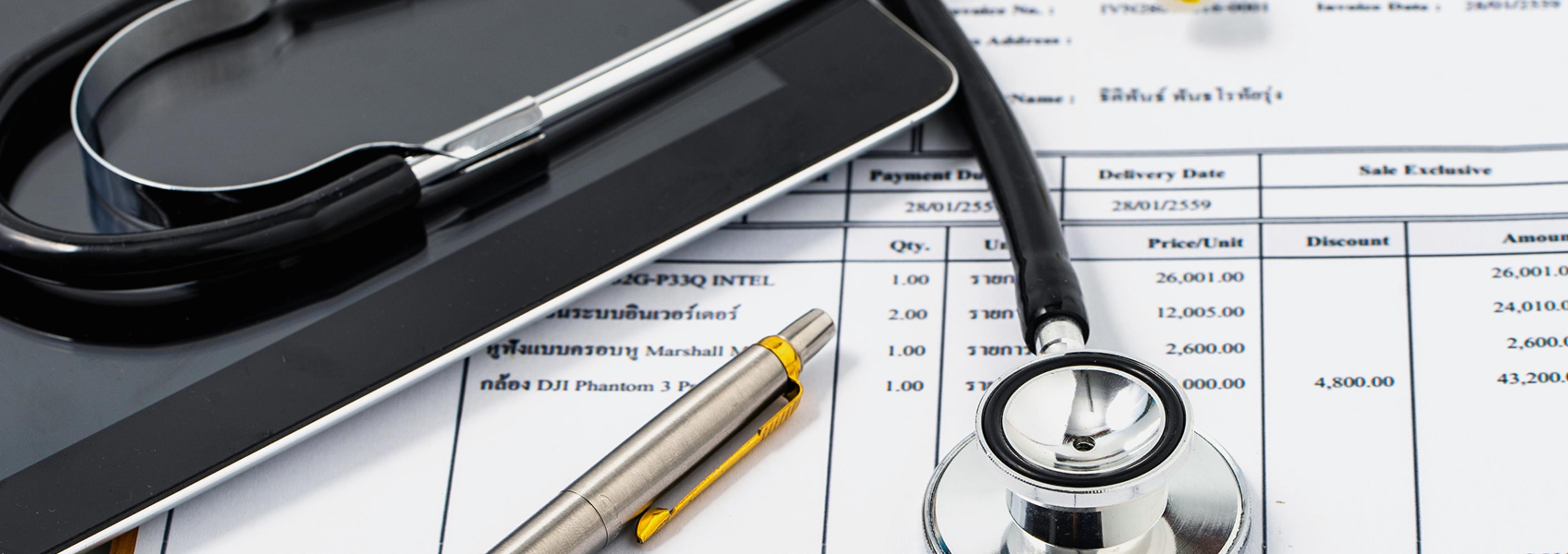 Close-up of a stethoscope, a pen with a yellow clip, and a black pen placed on top of an invoice or medical document. The document includes itemized entries with quantities, descriptions in English and another language (likely Thai), unit prices, and totals