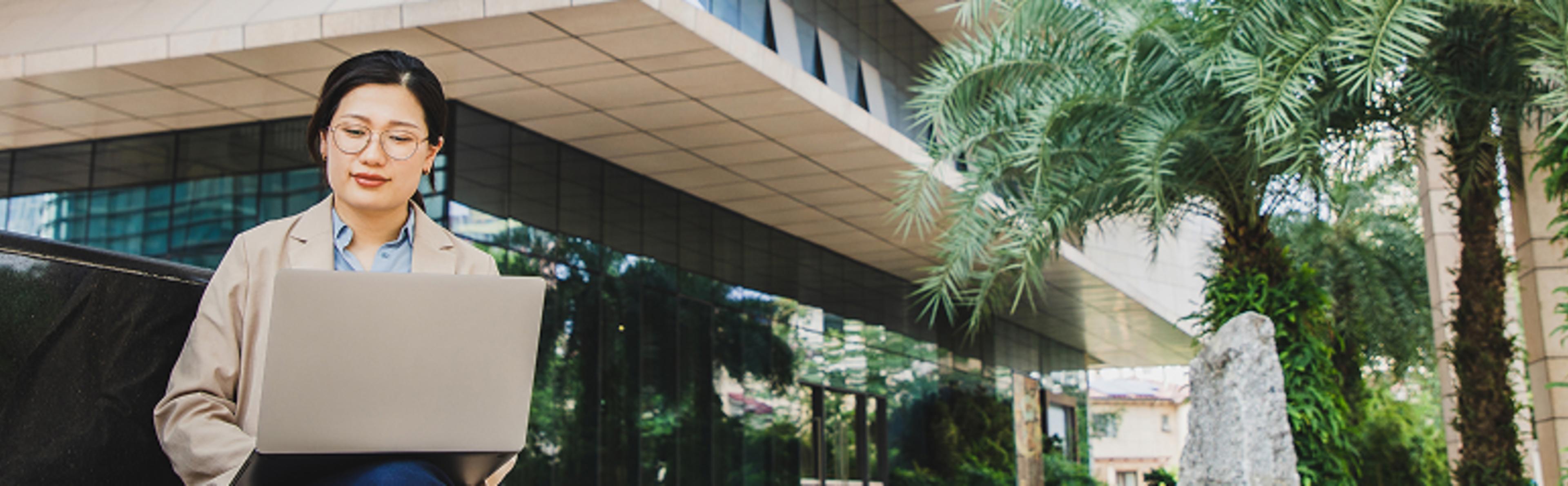 Business professional working on a laptop outdoors near a modern glass building and palm trees