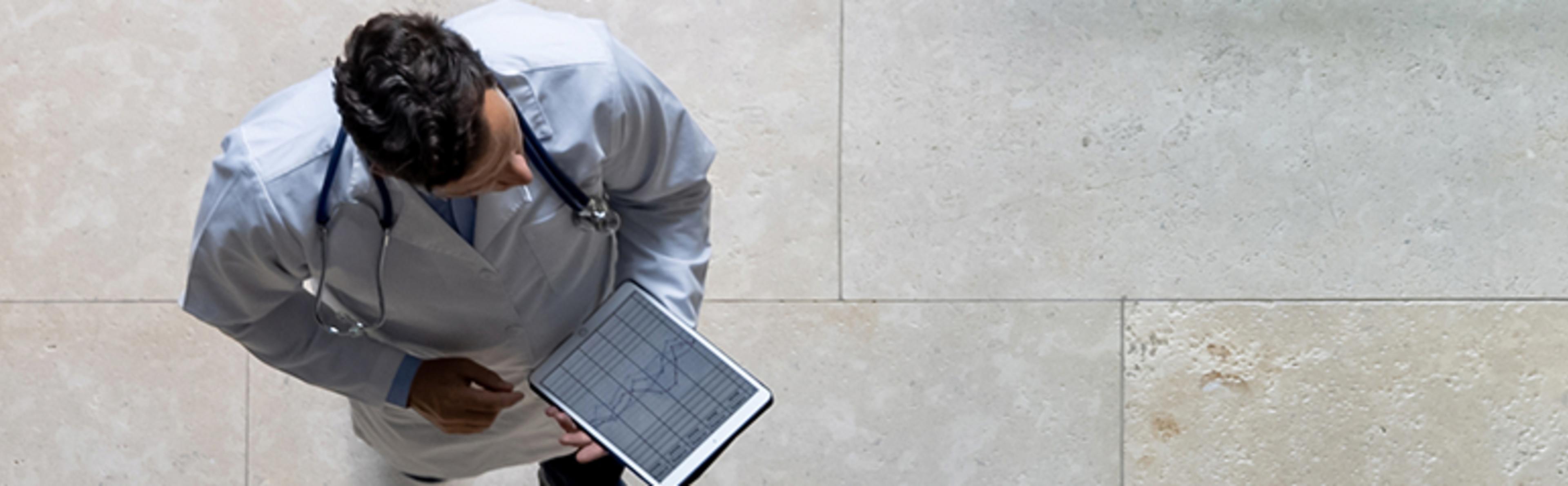 Individual in white coat holding tablet with graph, viewed from above