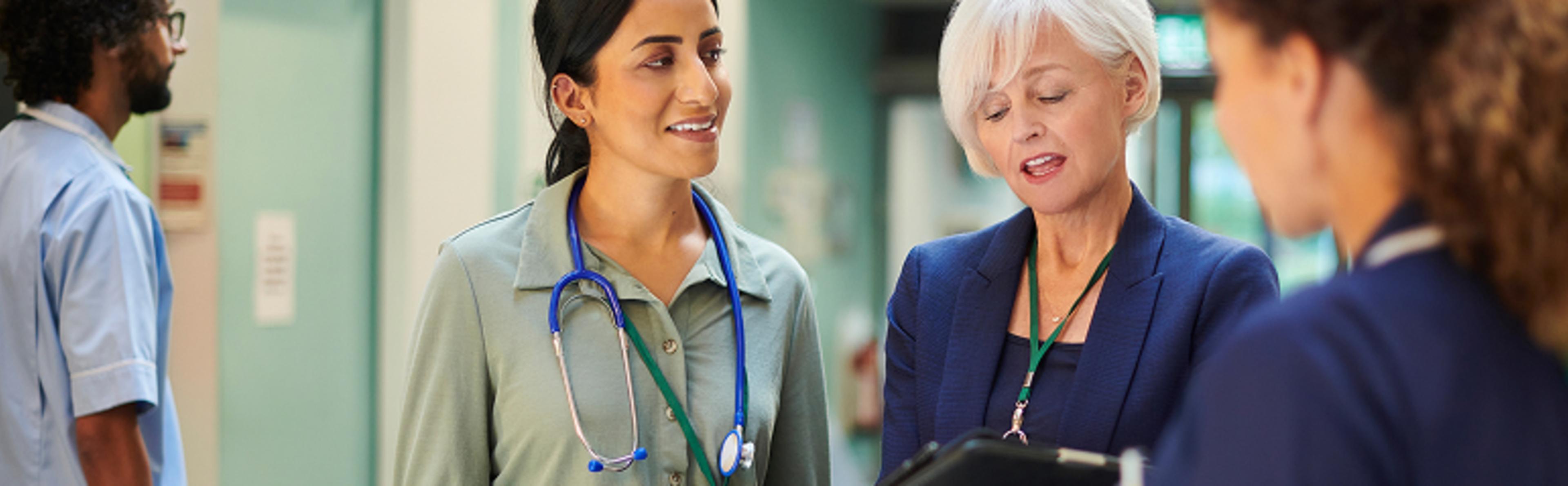 Two medical professionals collaborate with two executives, demonstrating information on a clipboard
