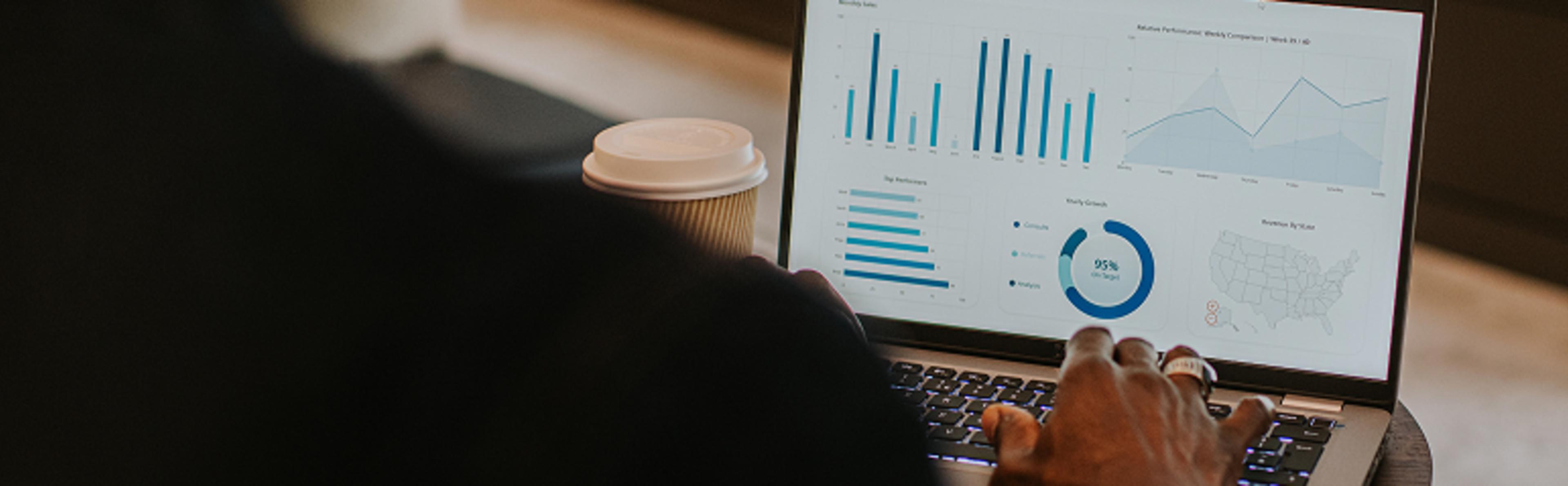 Laptop screen displays bar graphs, pie chart, and line graph; coffee cup placed nearby