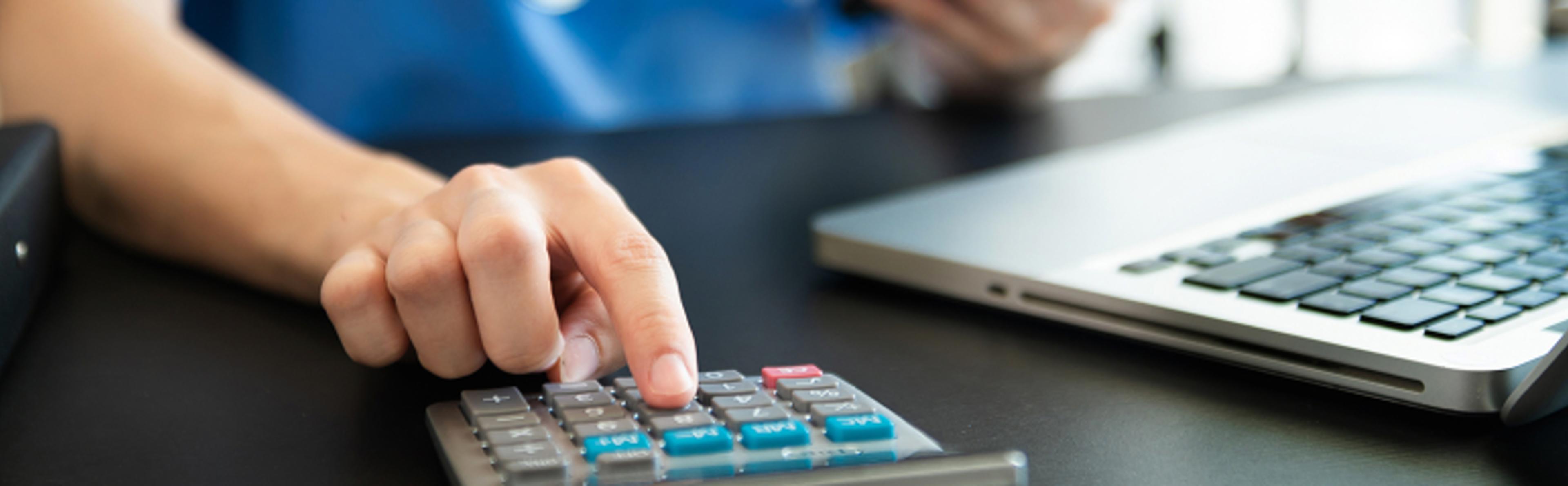 Hand pressing buttons on a calculator next to an open laptop on a black table