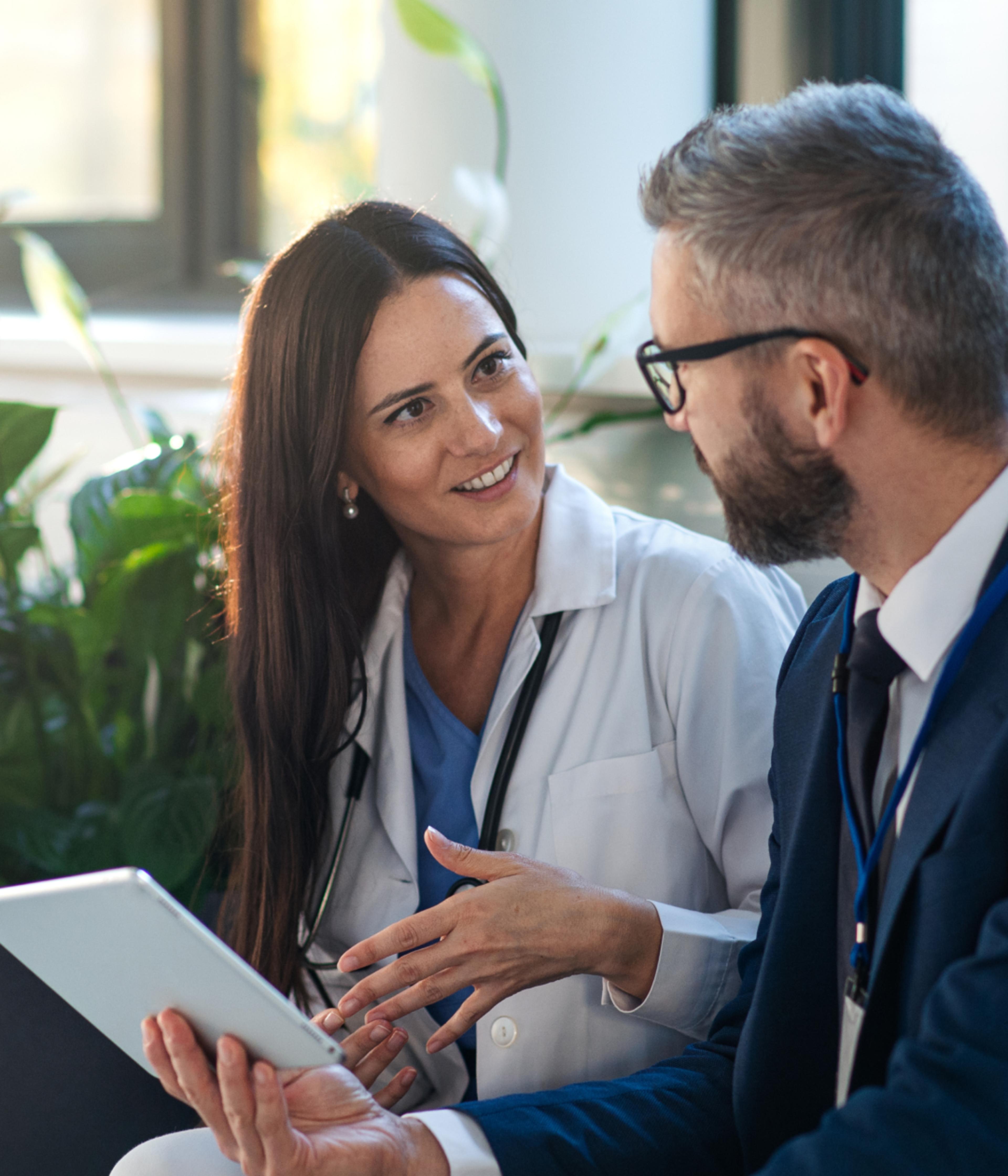 A doctor and a professional are discussing something while looking at a tablet