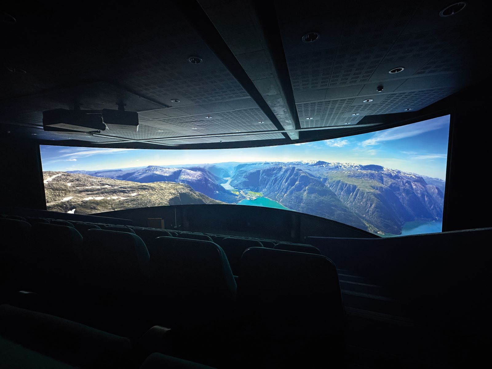 Panoramic movie theatre with lights off and a landscape photo on the screen.