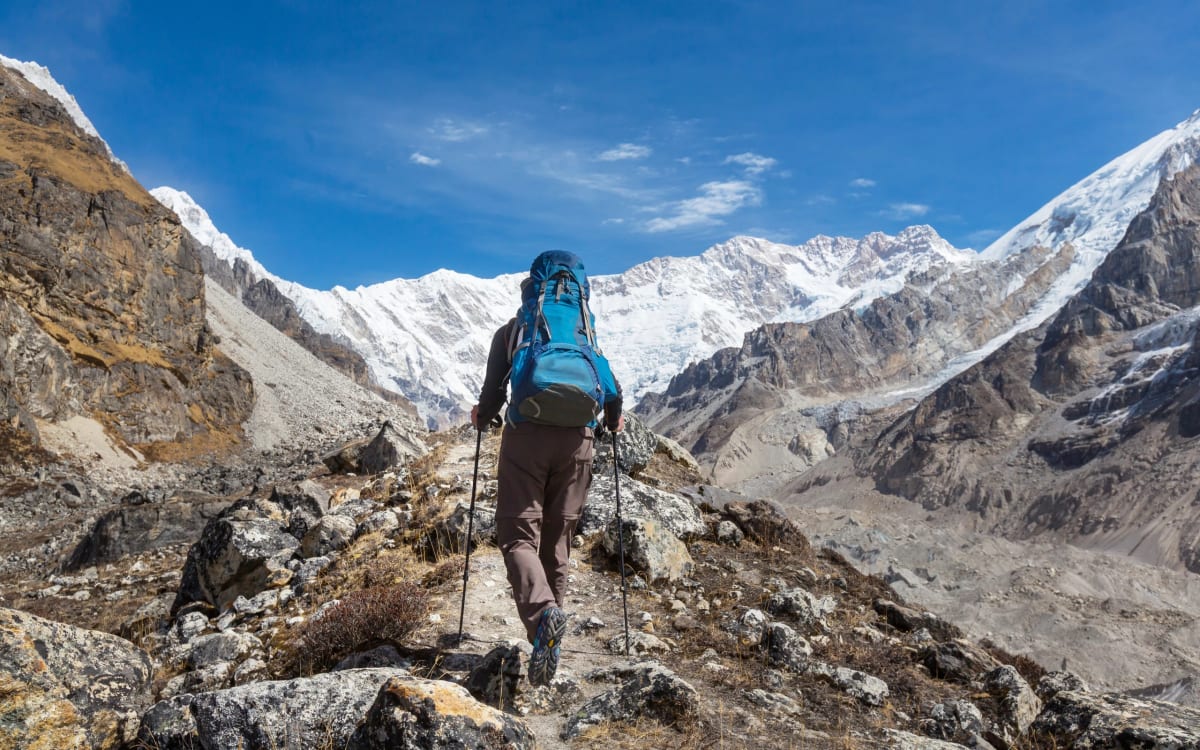 A hiker with poles below snow peaks