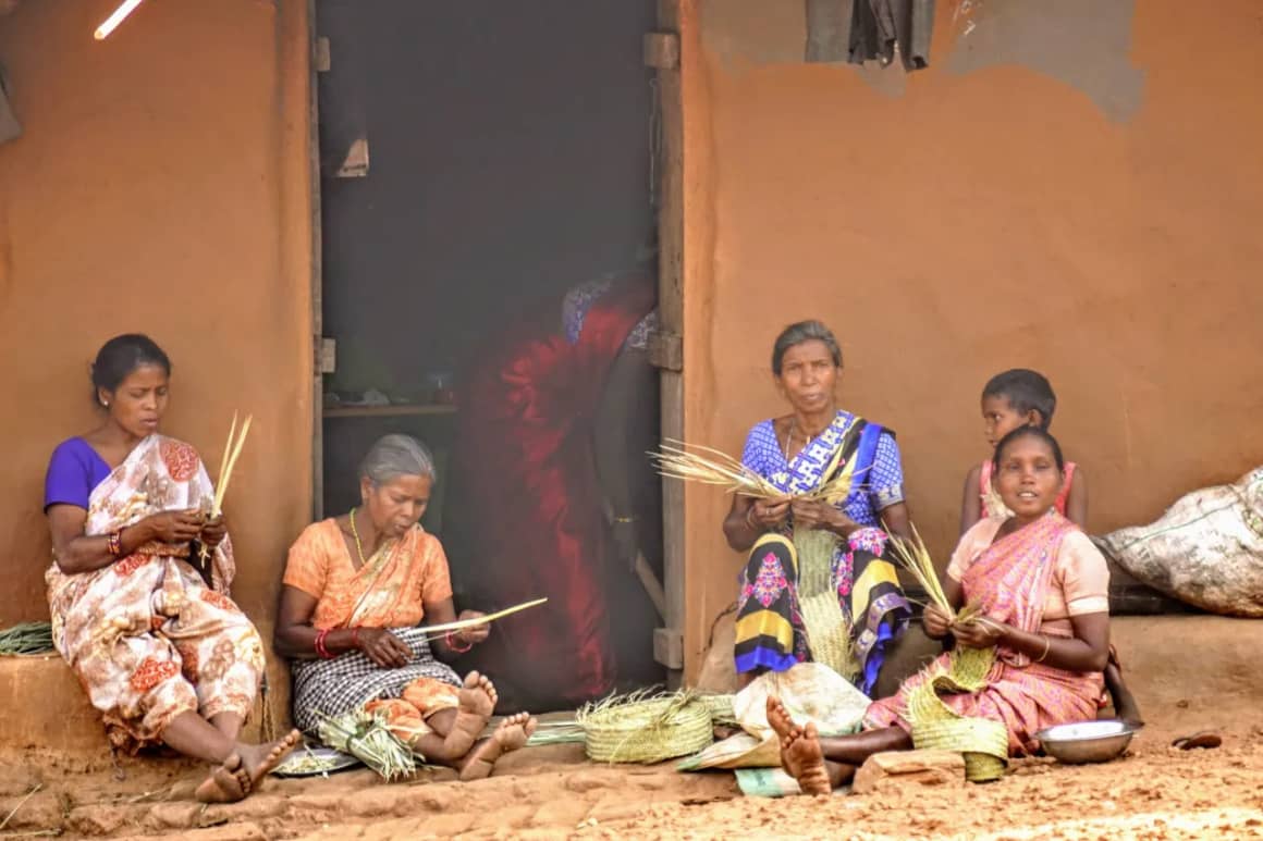 Tribal women weaving bamboo and forest produce crafts outside their home