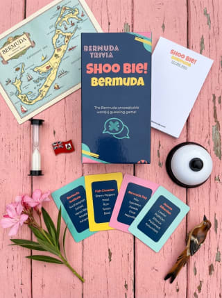 Shoo Bie! Bermuda game spread on a pink wood surface with cards, score pad, and props
