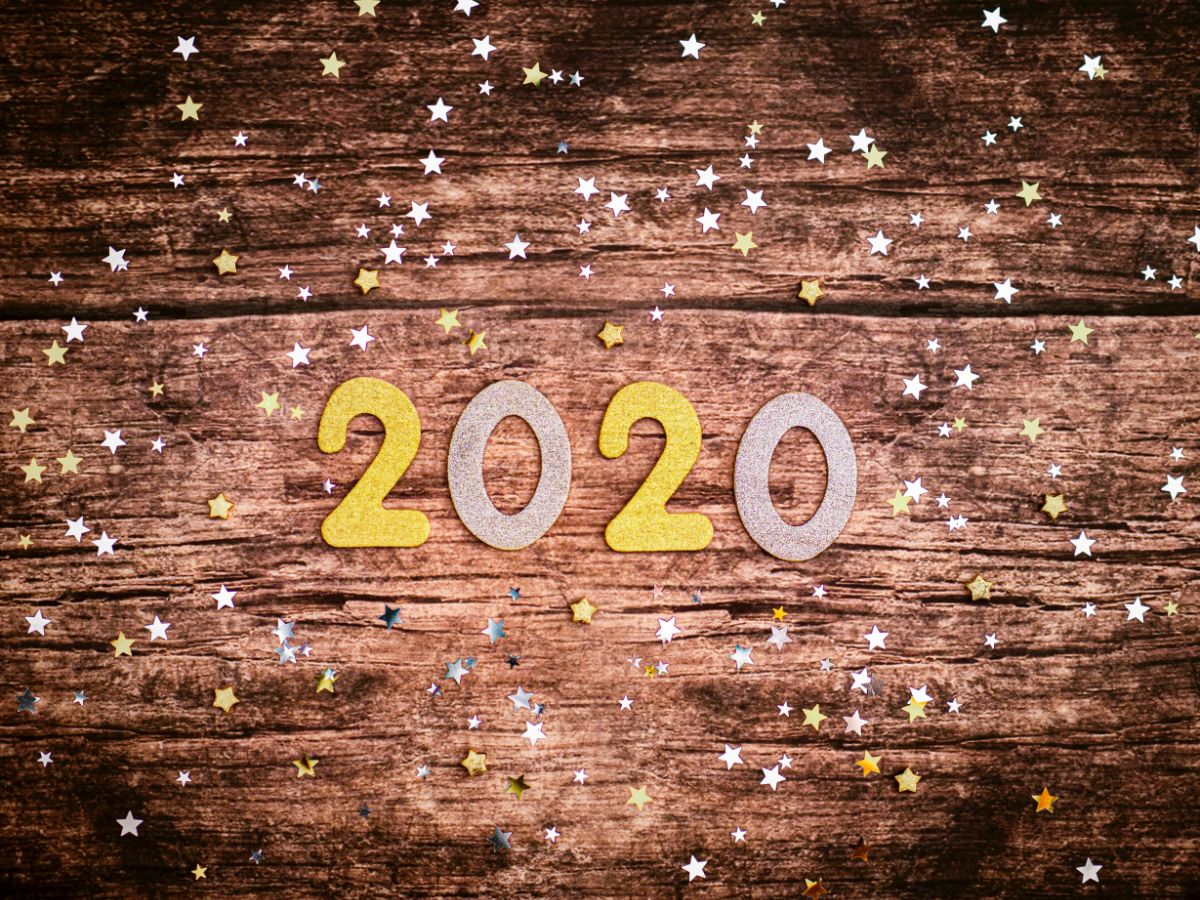 Paper or maybe felt '2020' and star confetti on a wood tabletop.