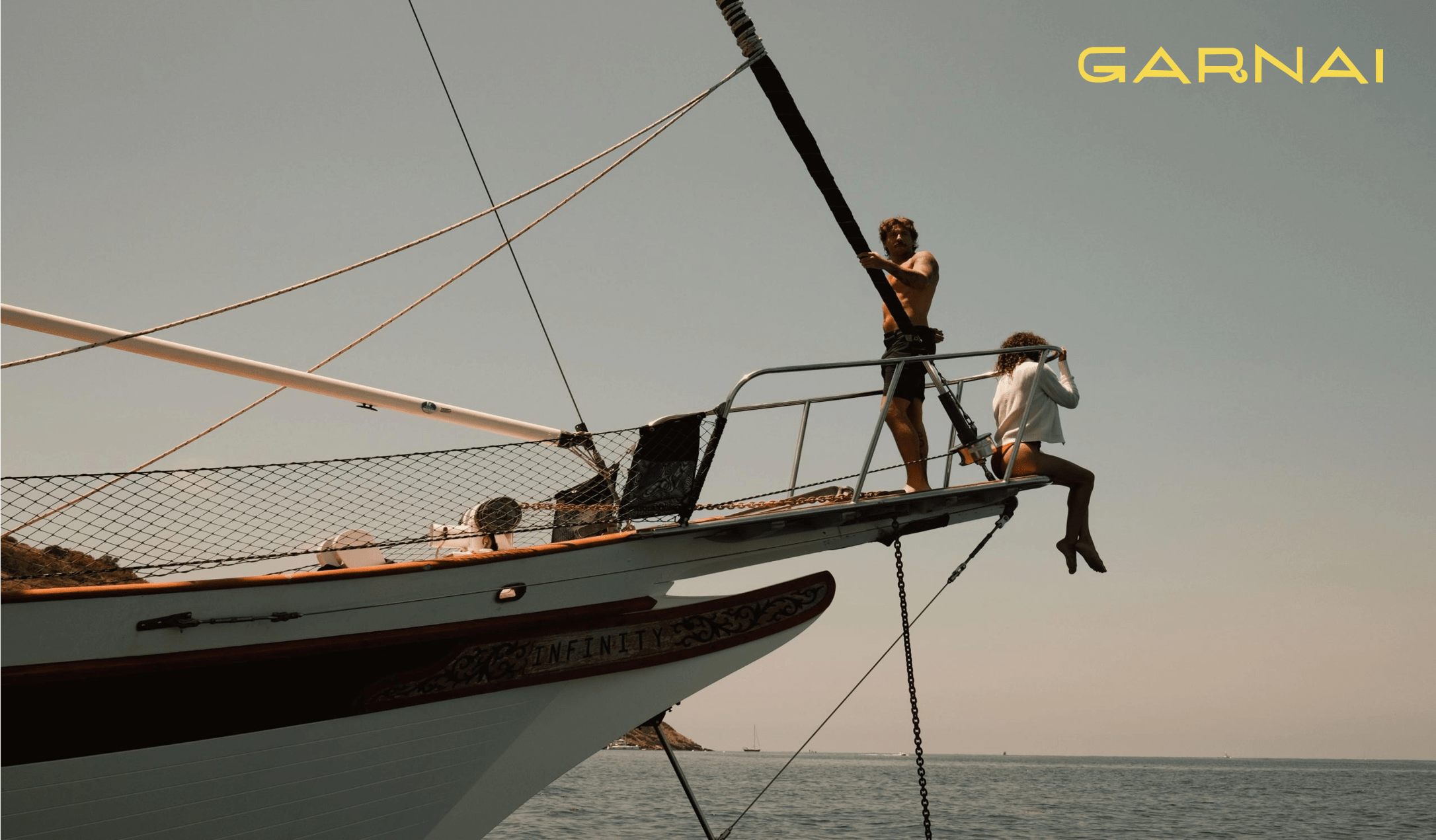 Two people out on the bowsprit of a sailing boat at sea