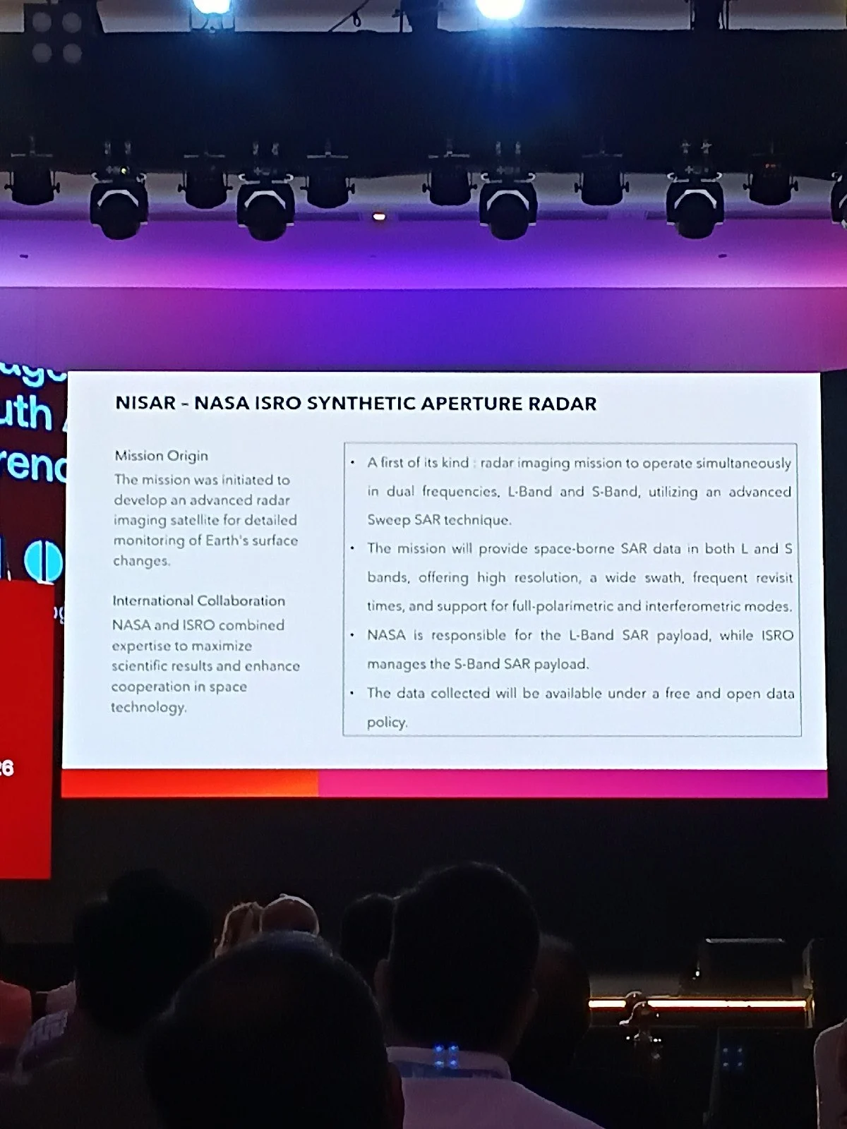 A conference slide about the NISAR NASA ISRO Synthetic Aperture Radar mission is shown on a large screen above a seated audience.