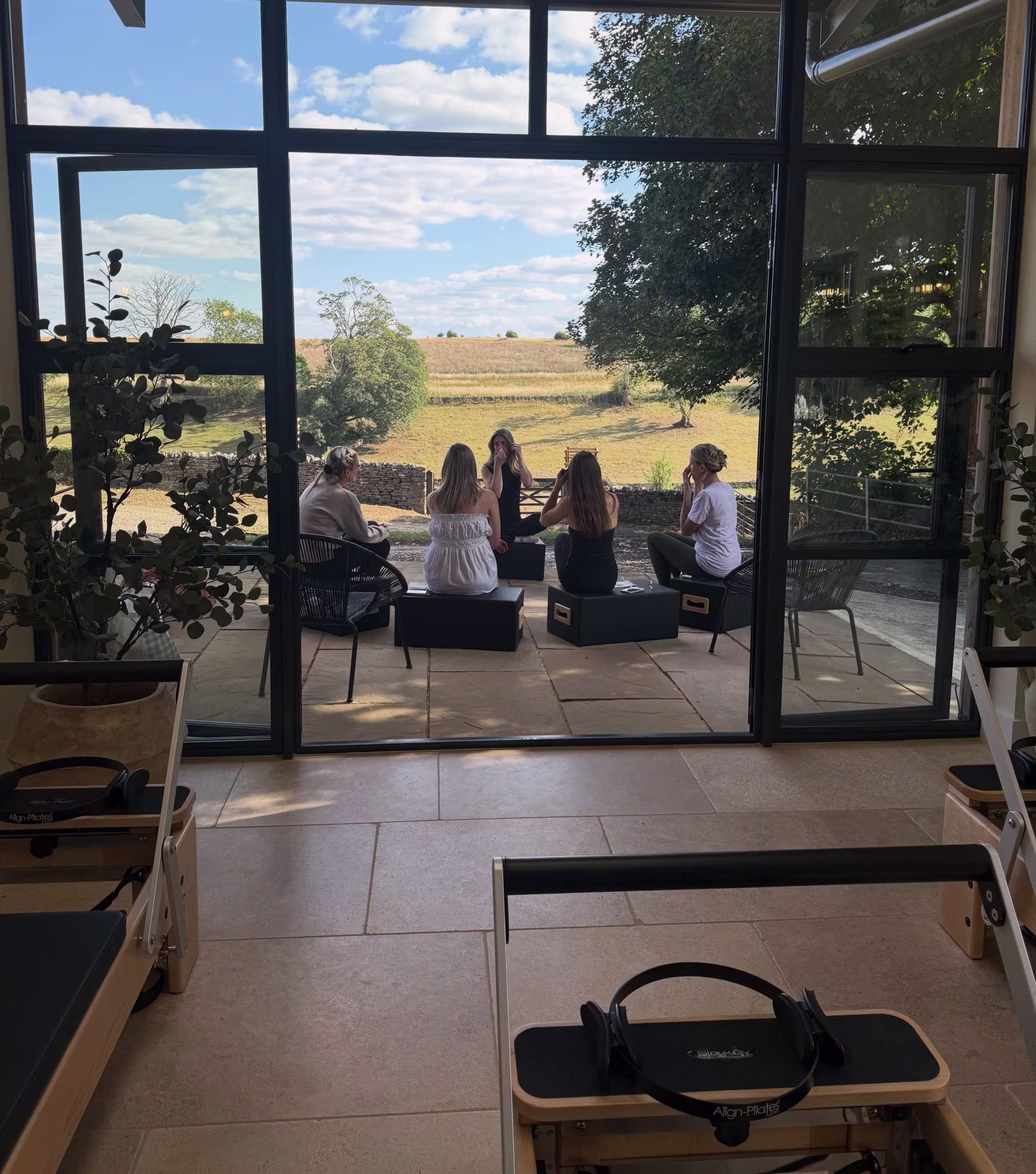 Inside the Reformer Room studio and a private group hire wellness day, with a view of the Cotswolds countryside through large windows.