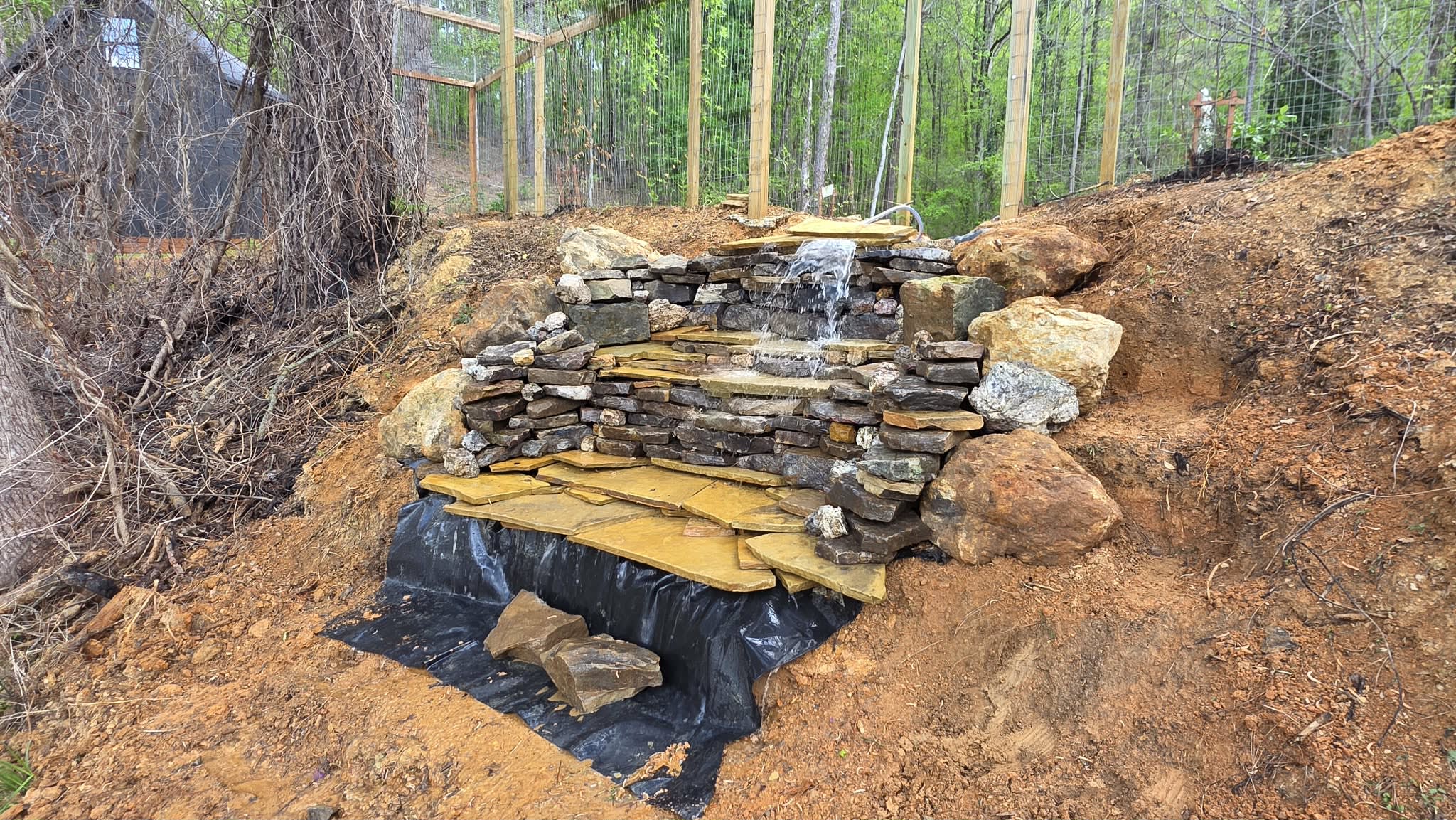 Chris hand-stacking the stone waterfall inside the vining pergola — in progress